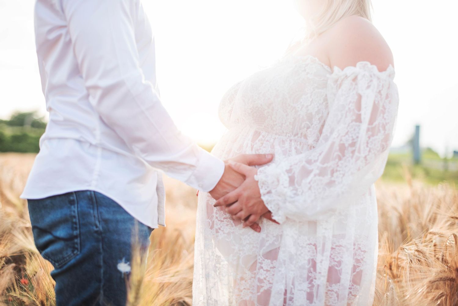 Maternity photo of couple in wheat field with sunlight and lace dress.