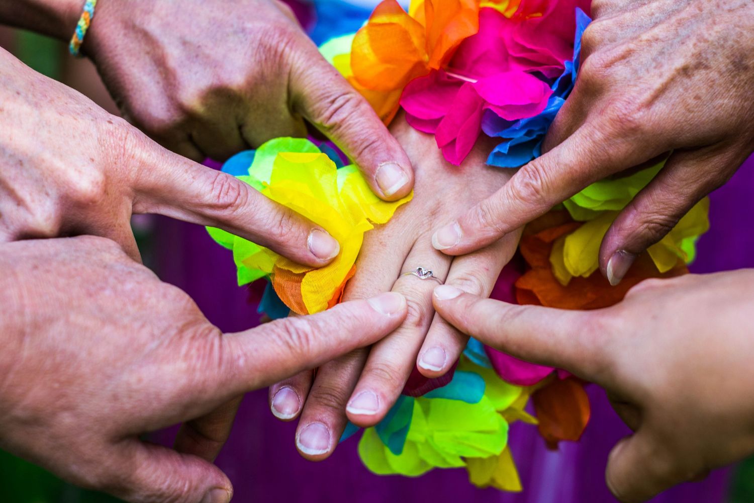 Colorful close-up of hands joining together over vibrant rainbow fabric.