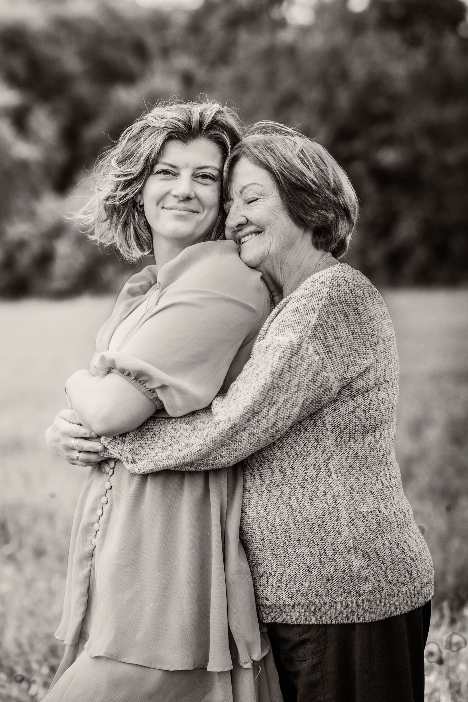 Black and white photo of two women sharing a warm embrace outdoors, smiling joyfully in a natural setting.