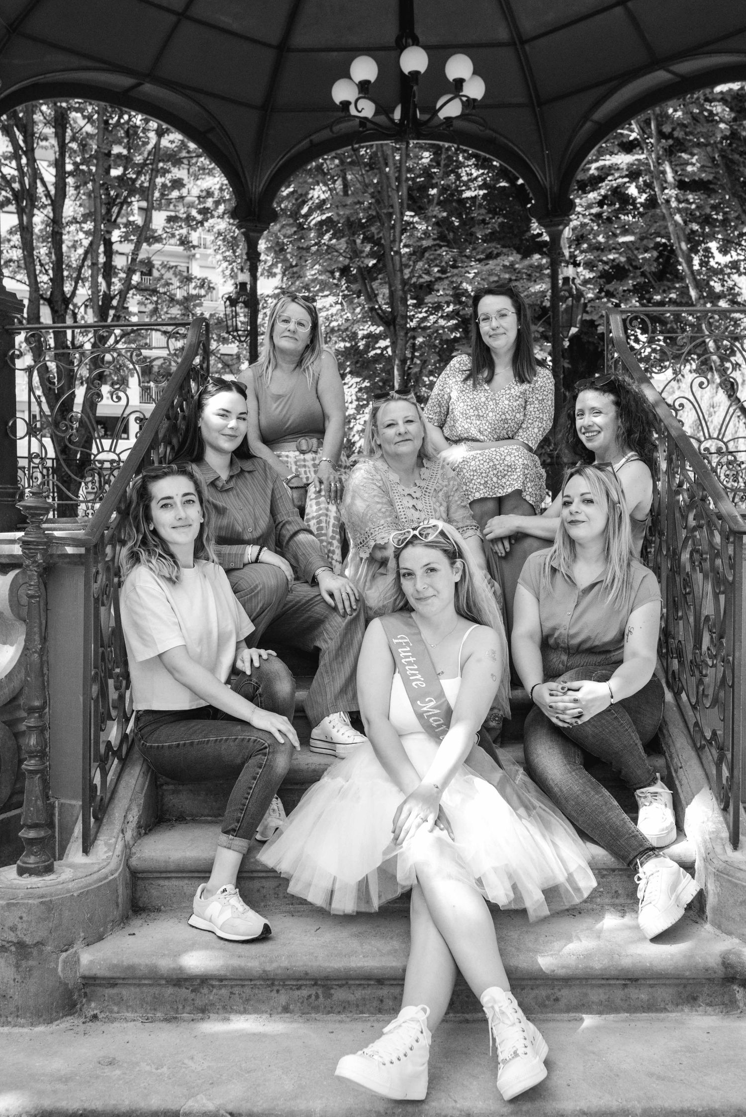 A group poses in a vintage-style black and white photo under an ornate gazebo.