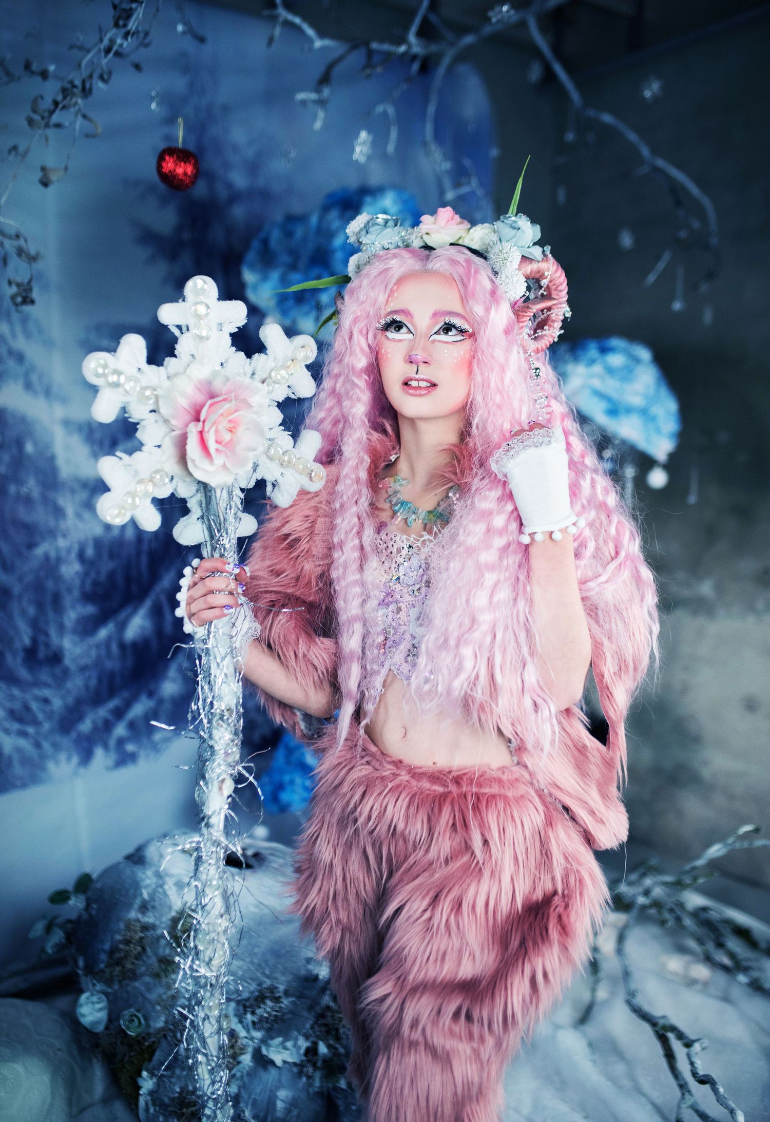 A figure in pink furry costume poses with ice sculptures in a whimsical winter scene.