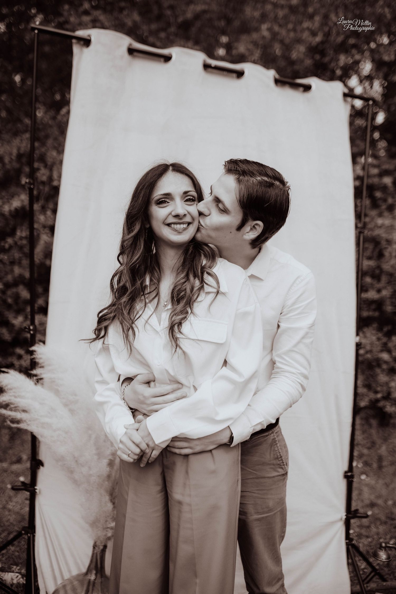 Sepia toned portrait of couple against white backdrop with pampas grass decor.