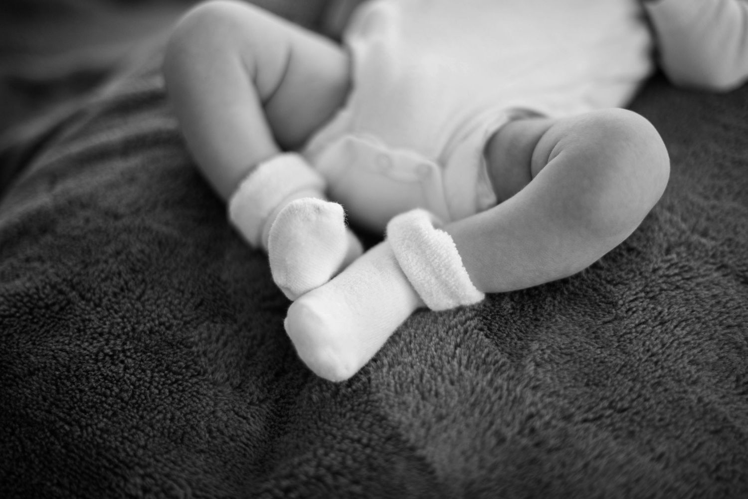 Black and white photos of sleeping baby in white clothing on dark textured blanket.