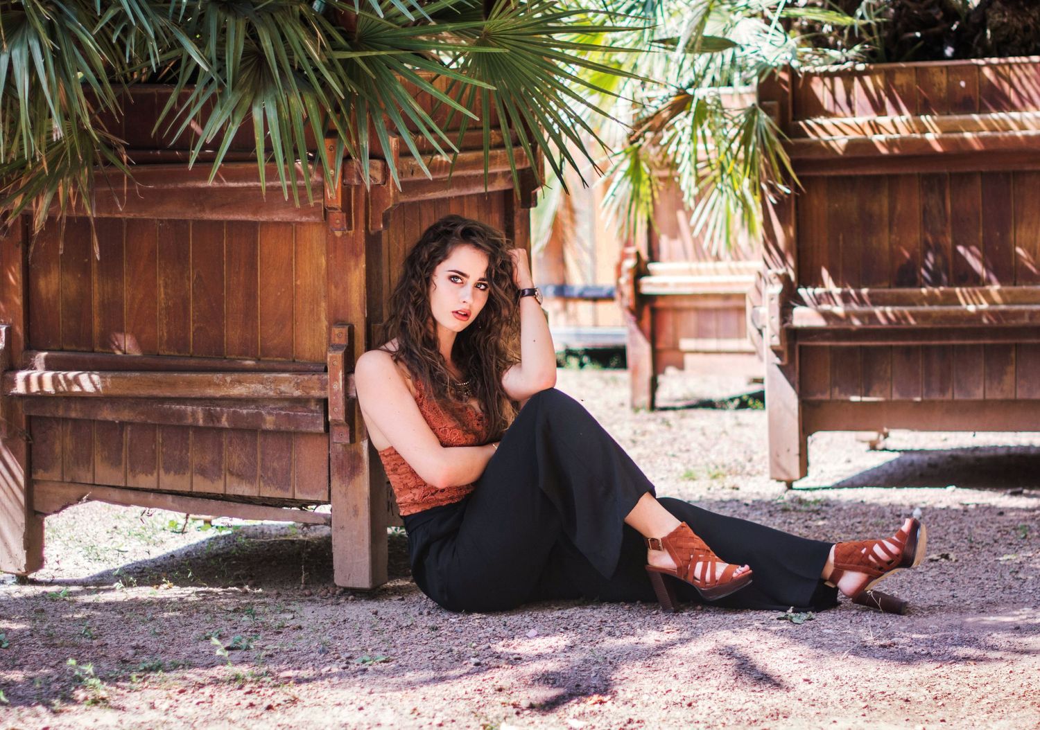 Casual portrait of someone relaxing outdoors against wooden backdrop with palm trees.