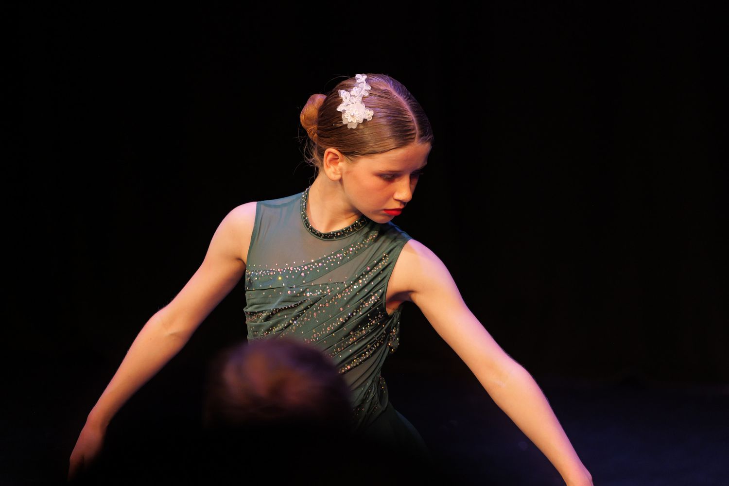 Young female dancer in green dress with hair accessory performs gracefully on a dimly lit stage. Dance show