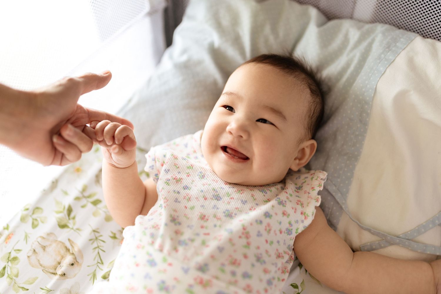 Happy smiling baby lying down reaching up to hold an adult finger.