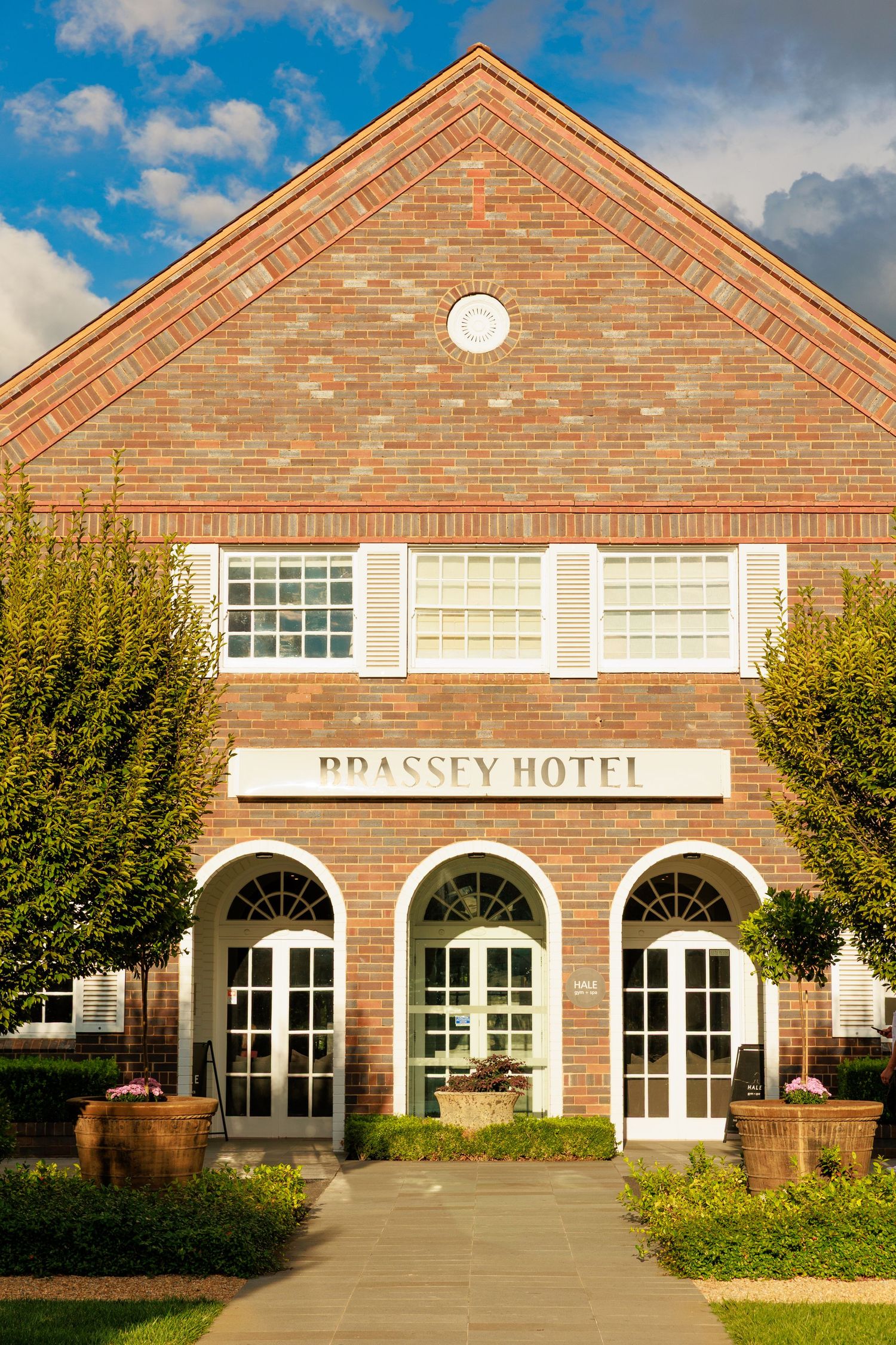 Exterior of elegant Brassey Hotel brick building with arched windows and manicured garden entrance.