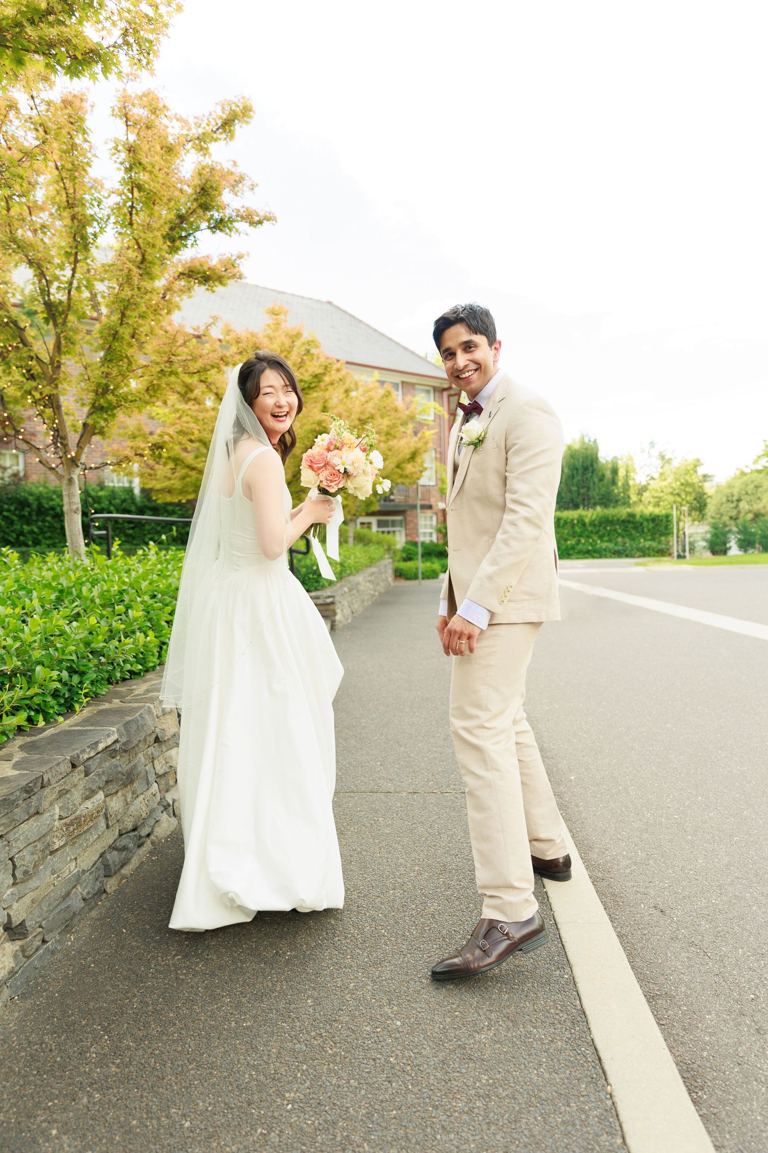 Joyful bride and groom posing on a tree-lined path on their wedding day outdoors.