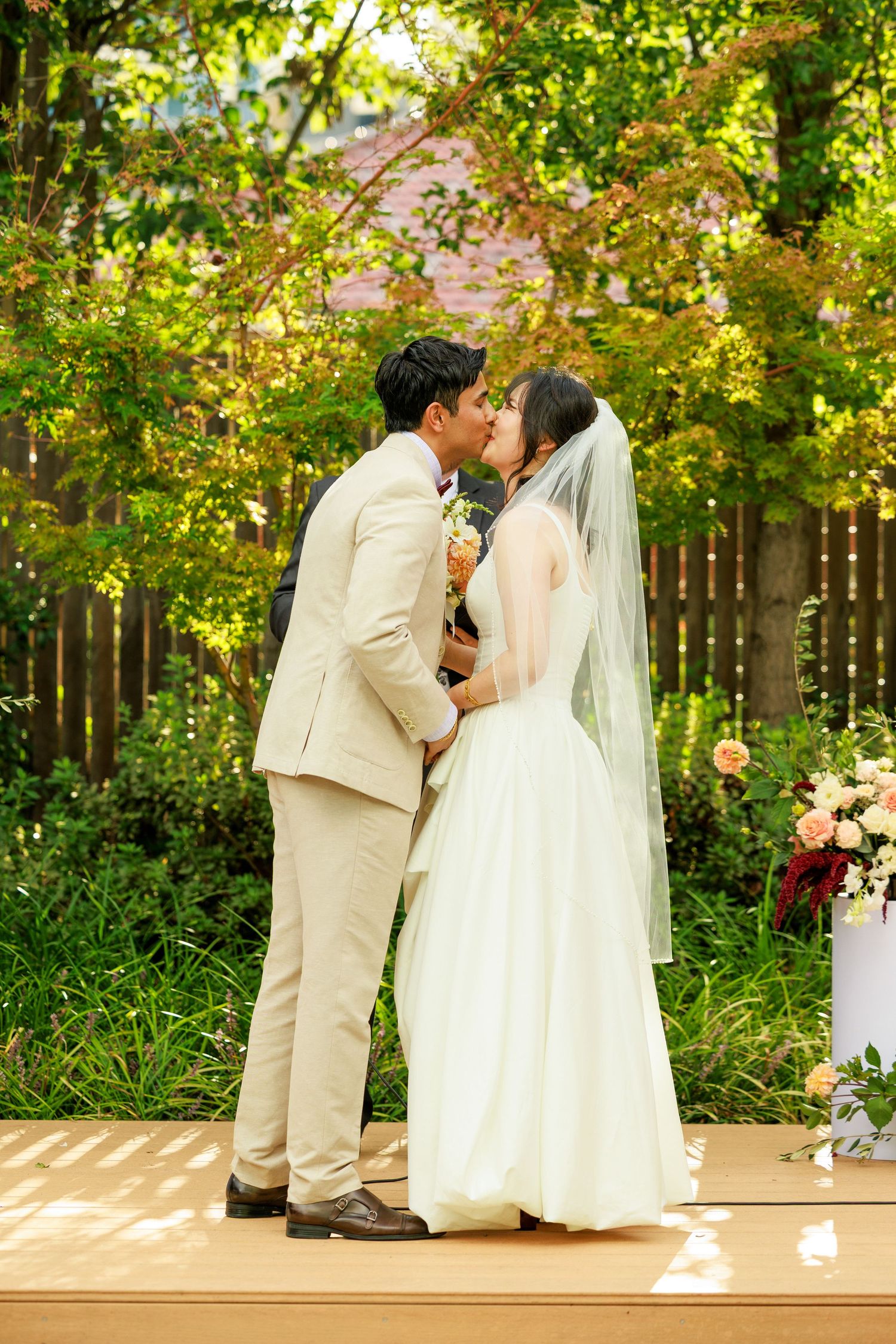 Asian couple shares first kiss as newlyweds at outdoor garden wedding ceremony.