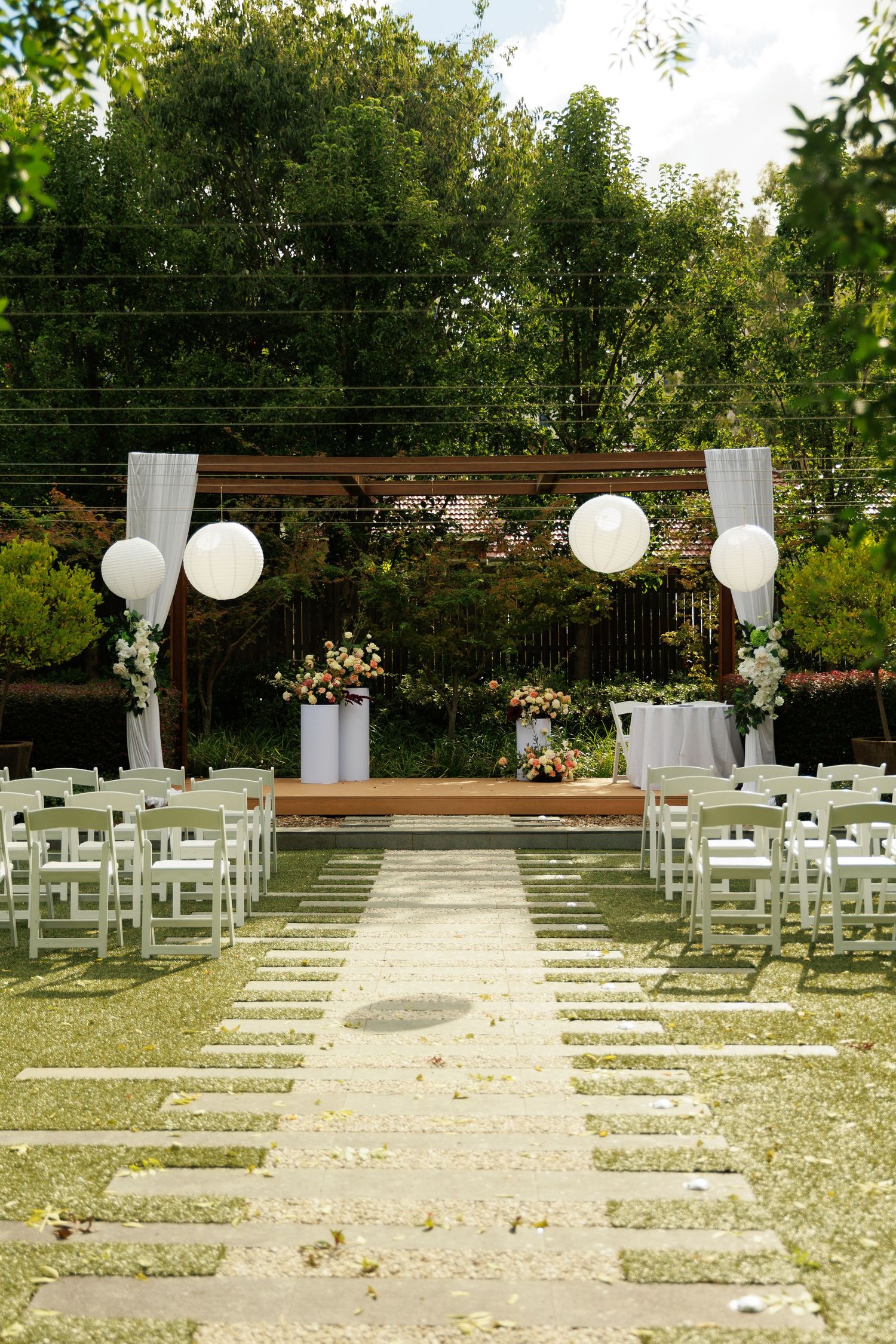 Beautiful outdoor wedding ceremony aisle with white chairs, large paper lanterns, and floral altar decorations.