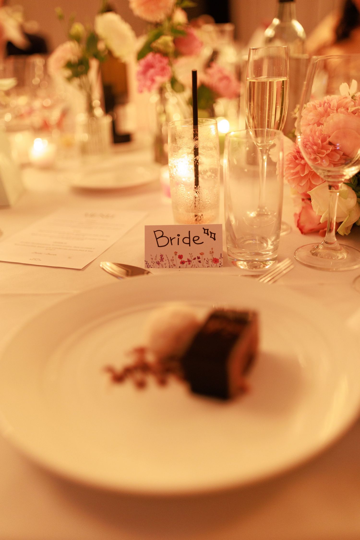 Bride place card at elegant wedding reception table setting with dessert, pink flowers and champagne.