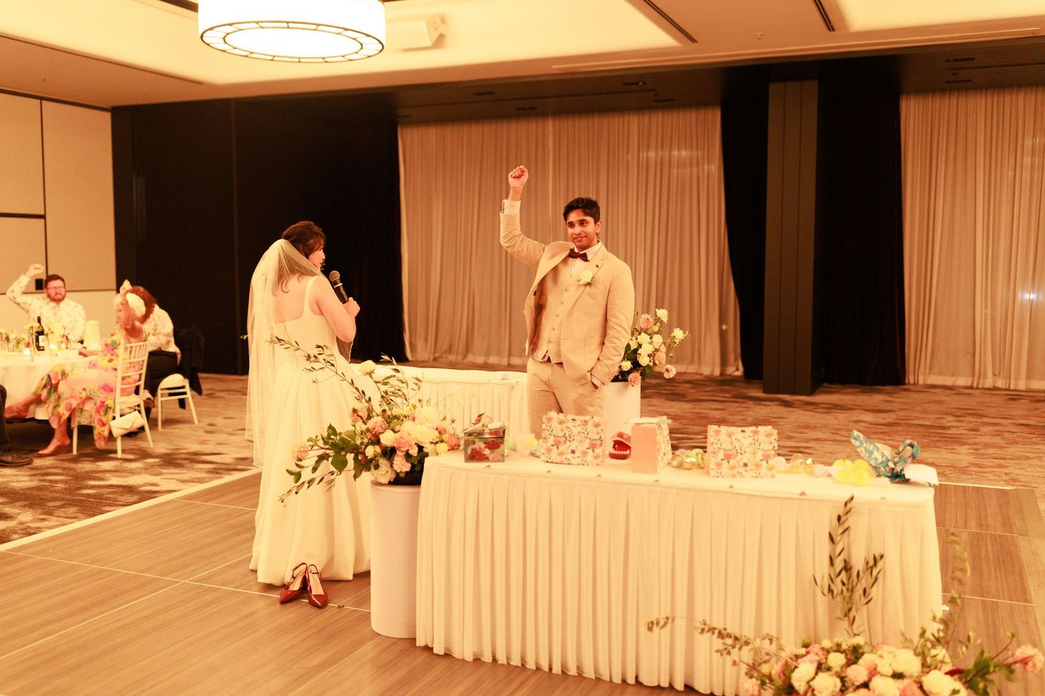 Bride and groom celebrating at wedding reception table decorated with white flowers in ballroom.