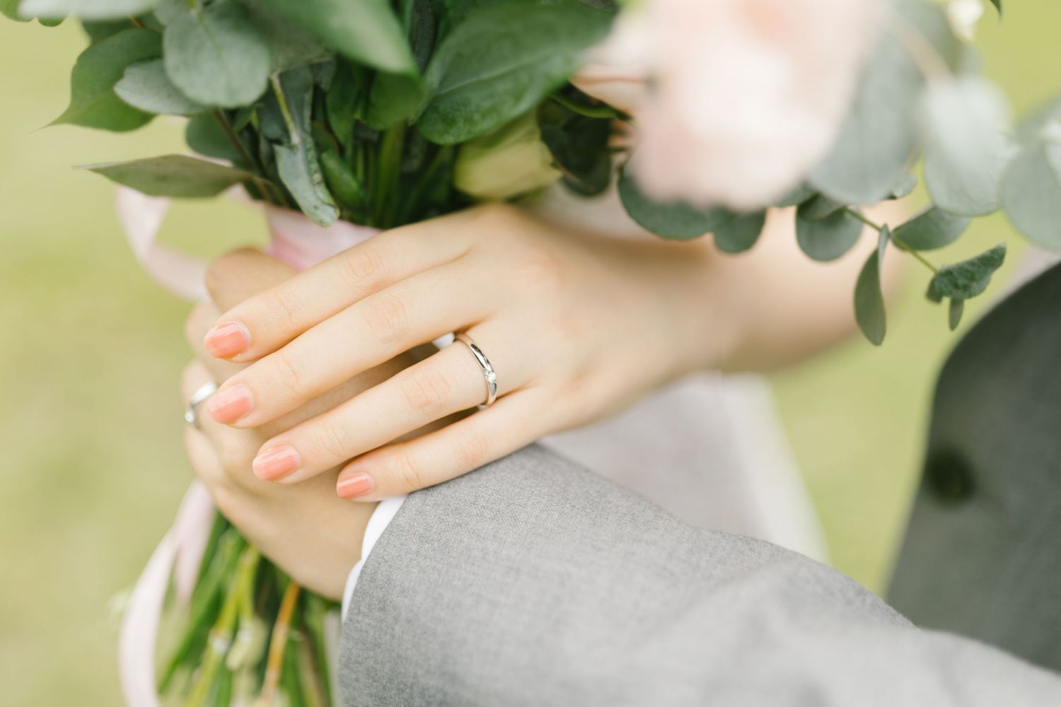 Close-up of bride and groom hands showing wedding rings with a floral bouquet.