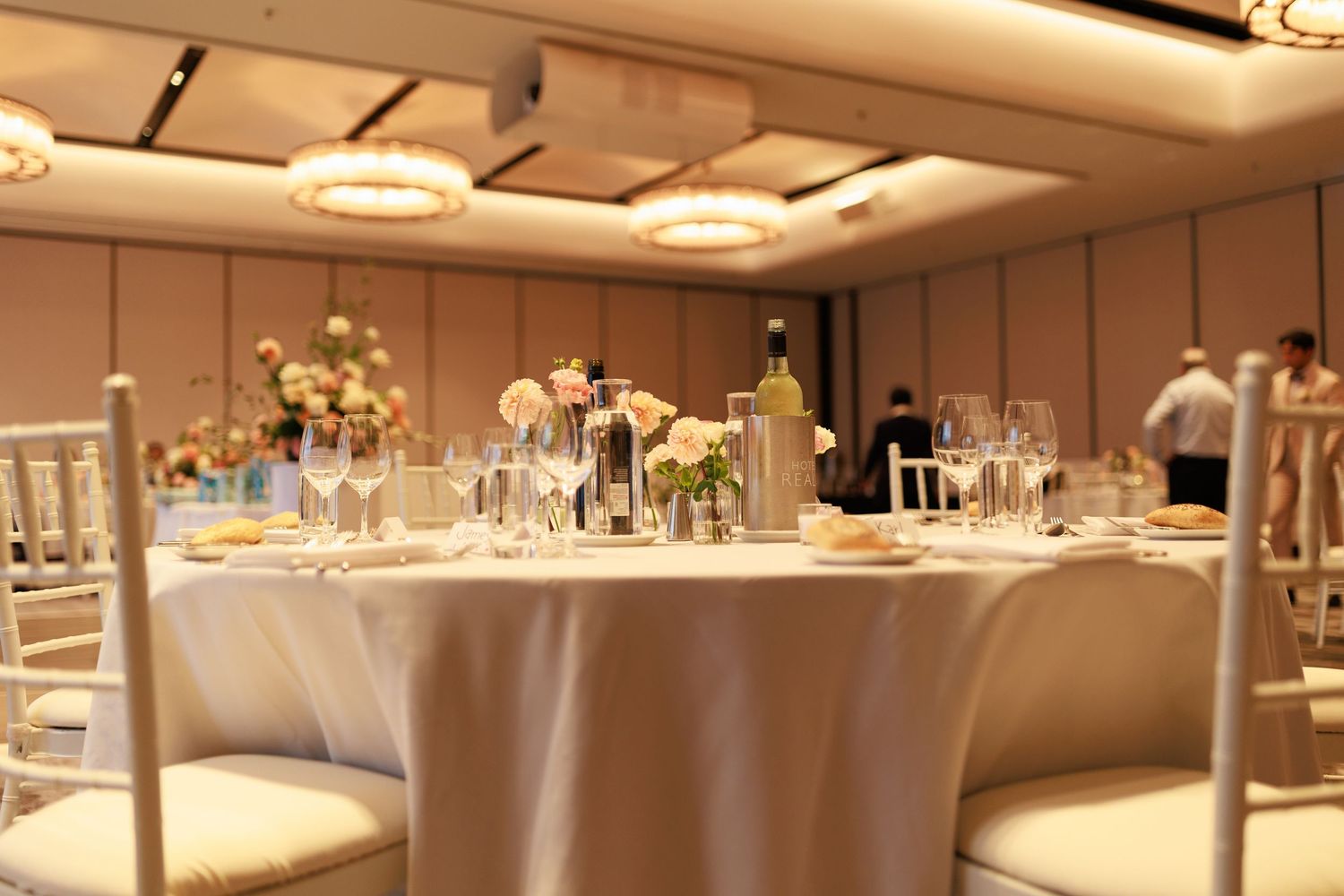 Elegant wedding reception ballroom with round tables, white linens, chiavari chairs and floral centerpieces.