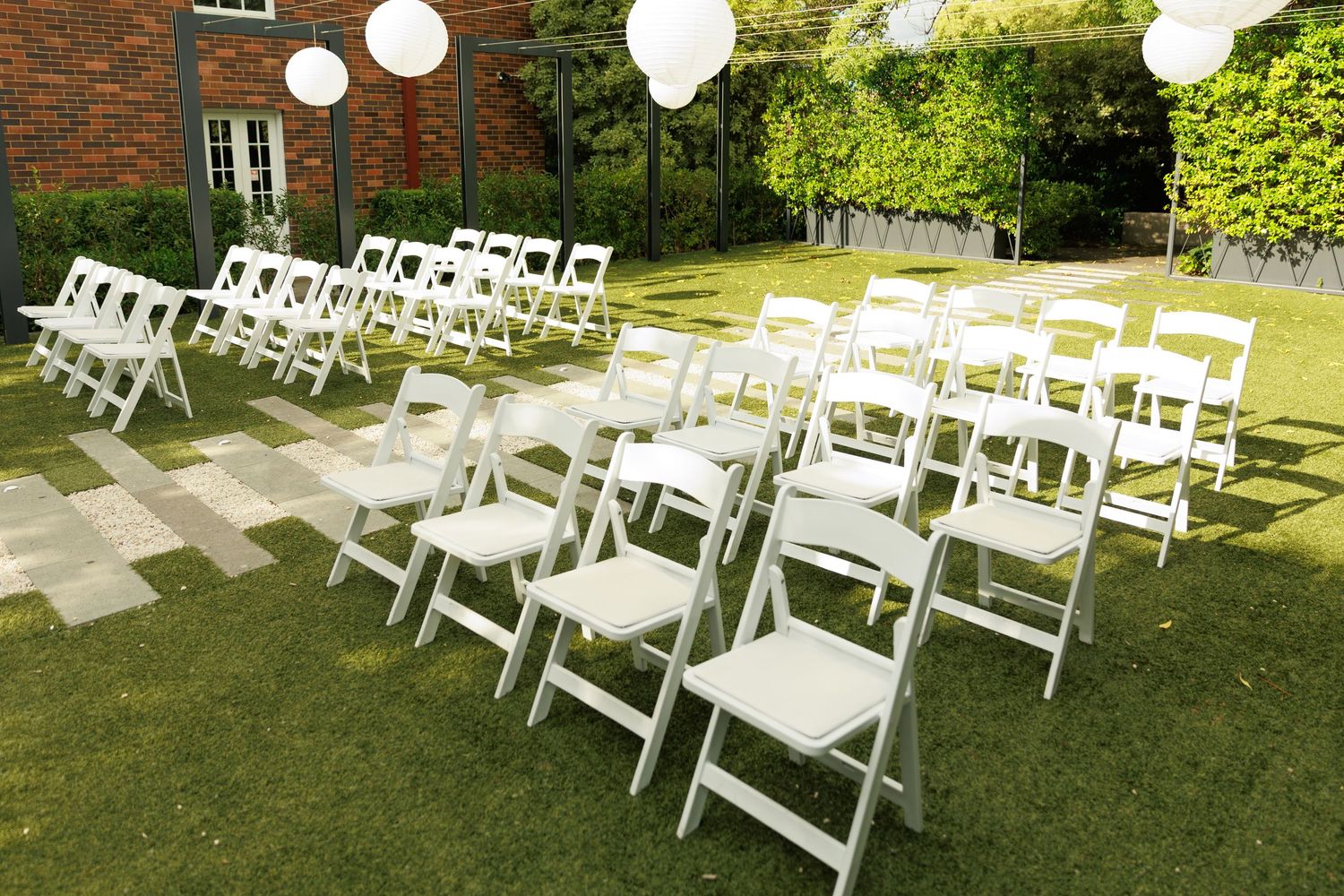Rows of white folding chairs arranged on green lawn for an outdoor garden wedding ceremony.