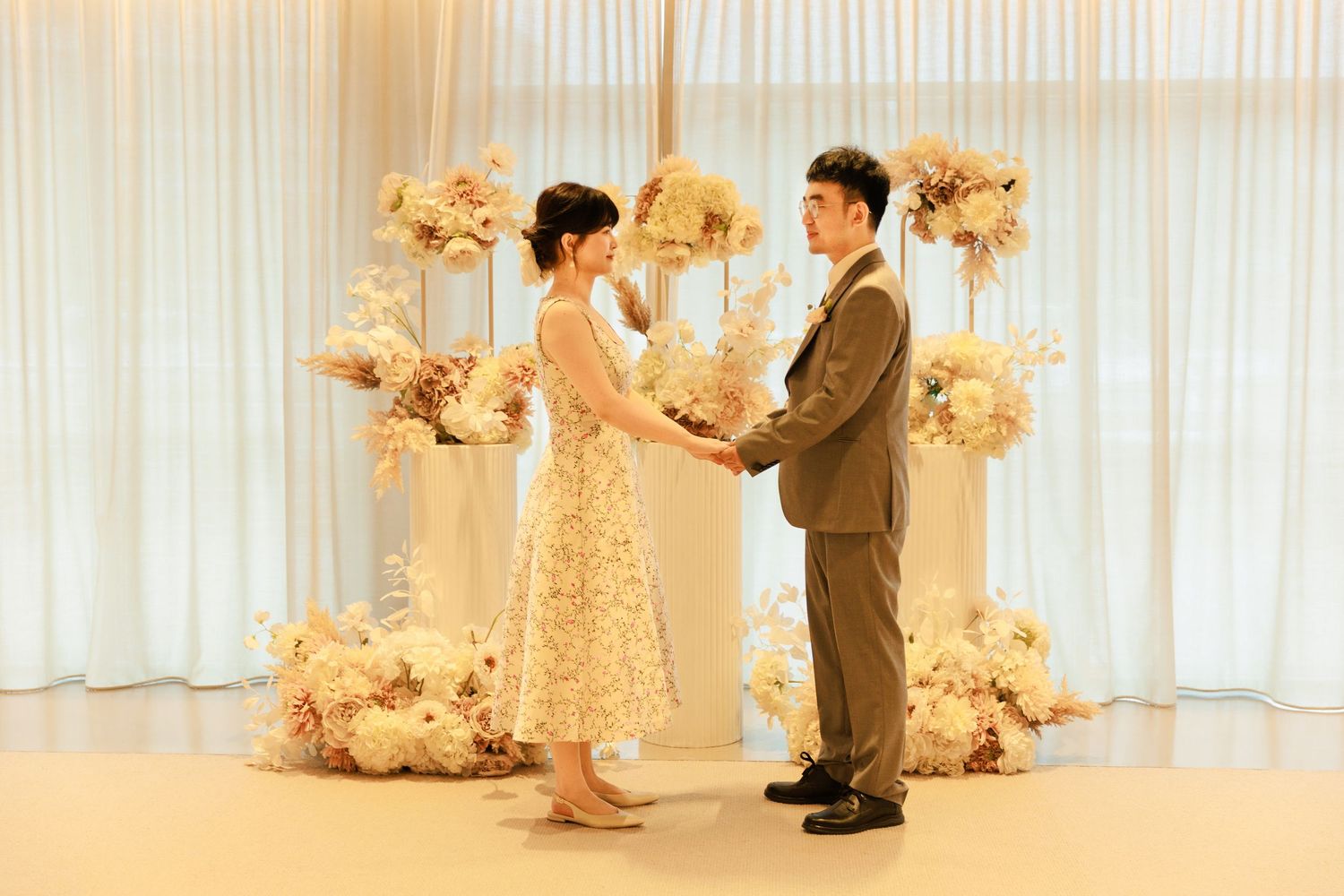 A couple holds hands and faces each other in a romantic wedding ceremony with elegant floral arrangements.