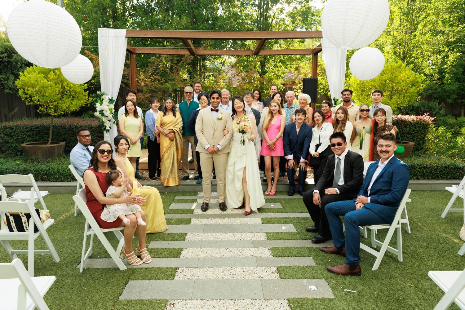 Wedding party and guests pose together at outdoor garden ceremony with white balloon decor.