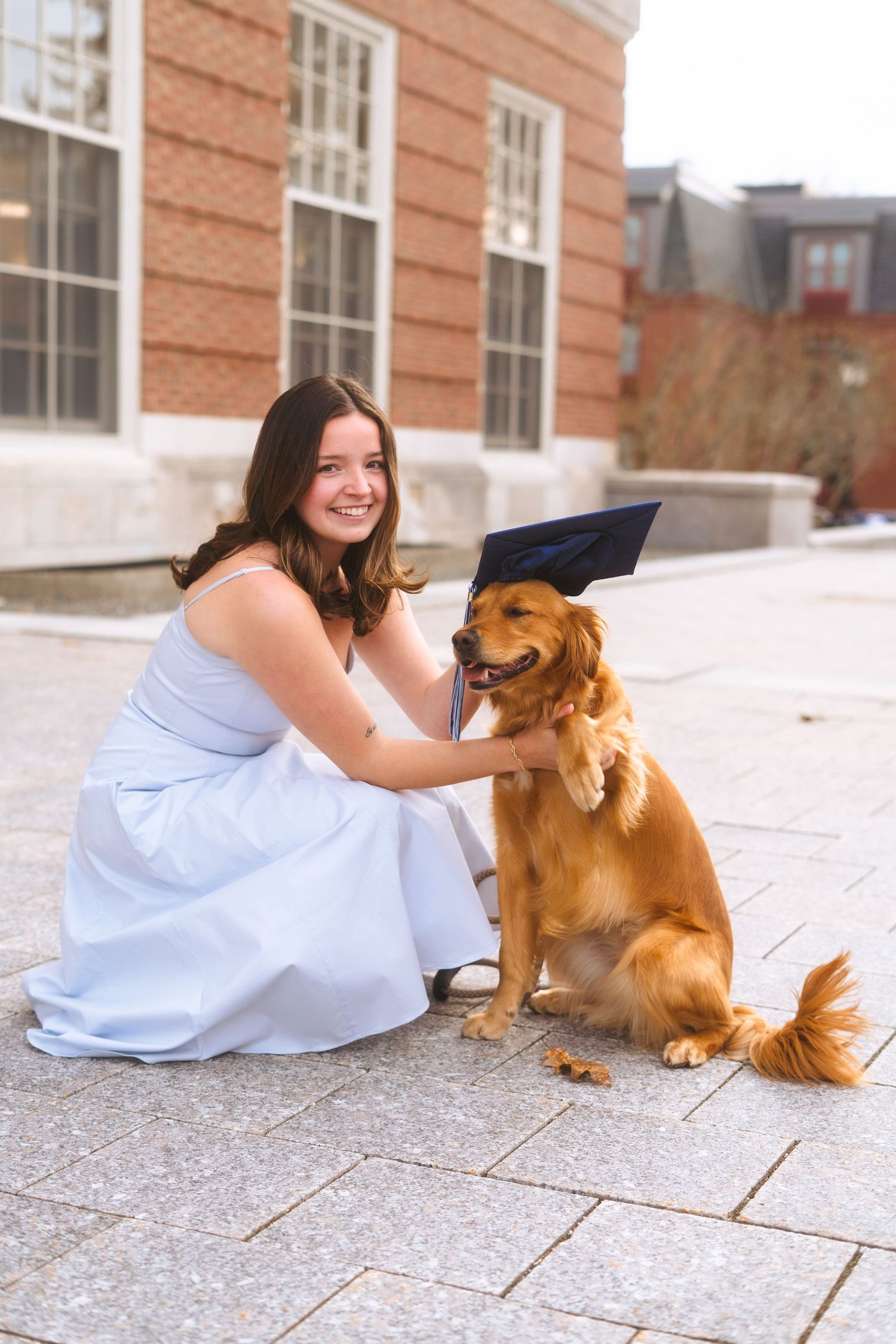 girl placing graduation cap on dogs head and smiling