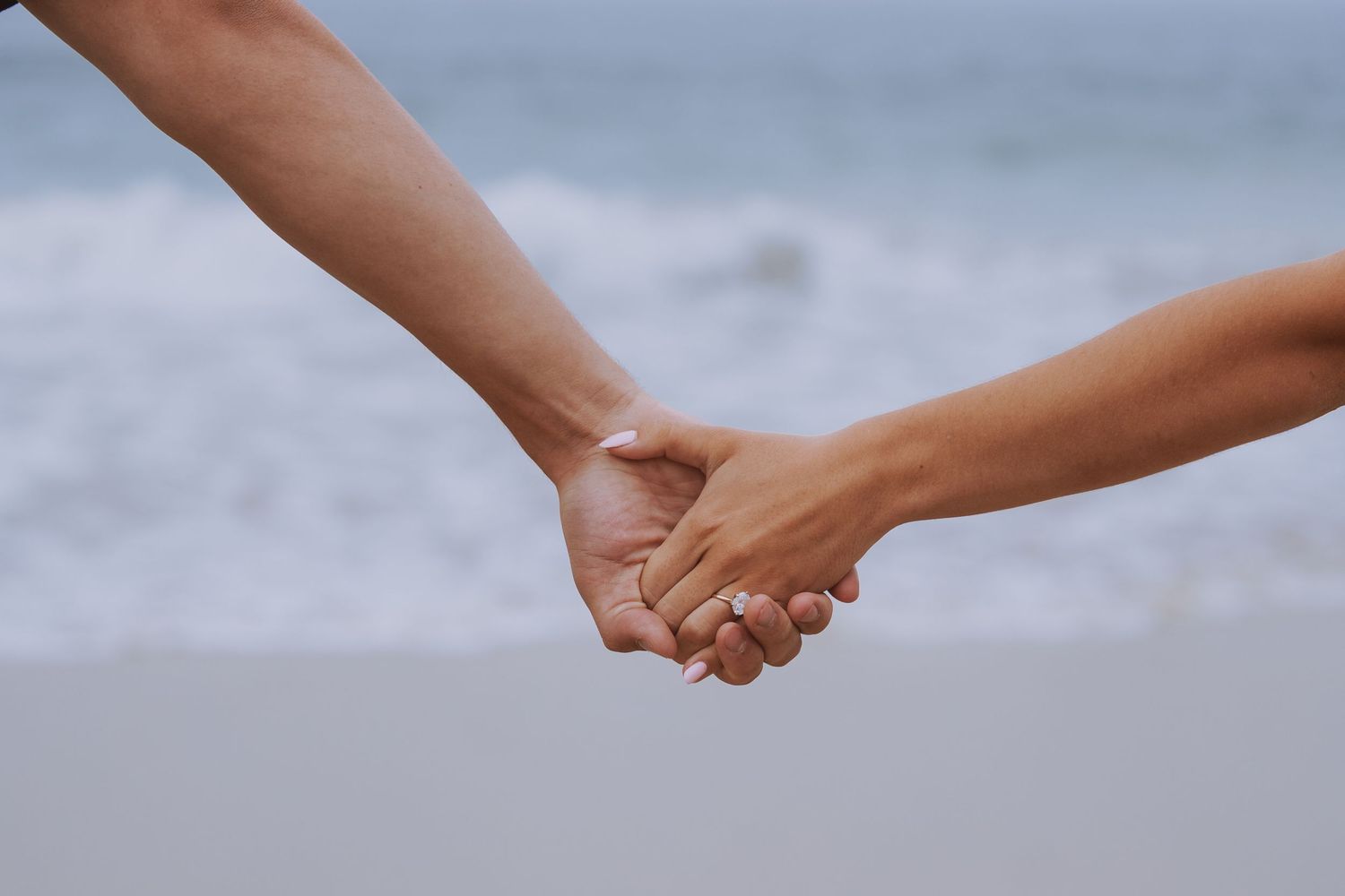 two hands holding in front of ocean