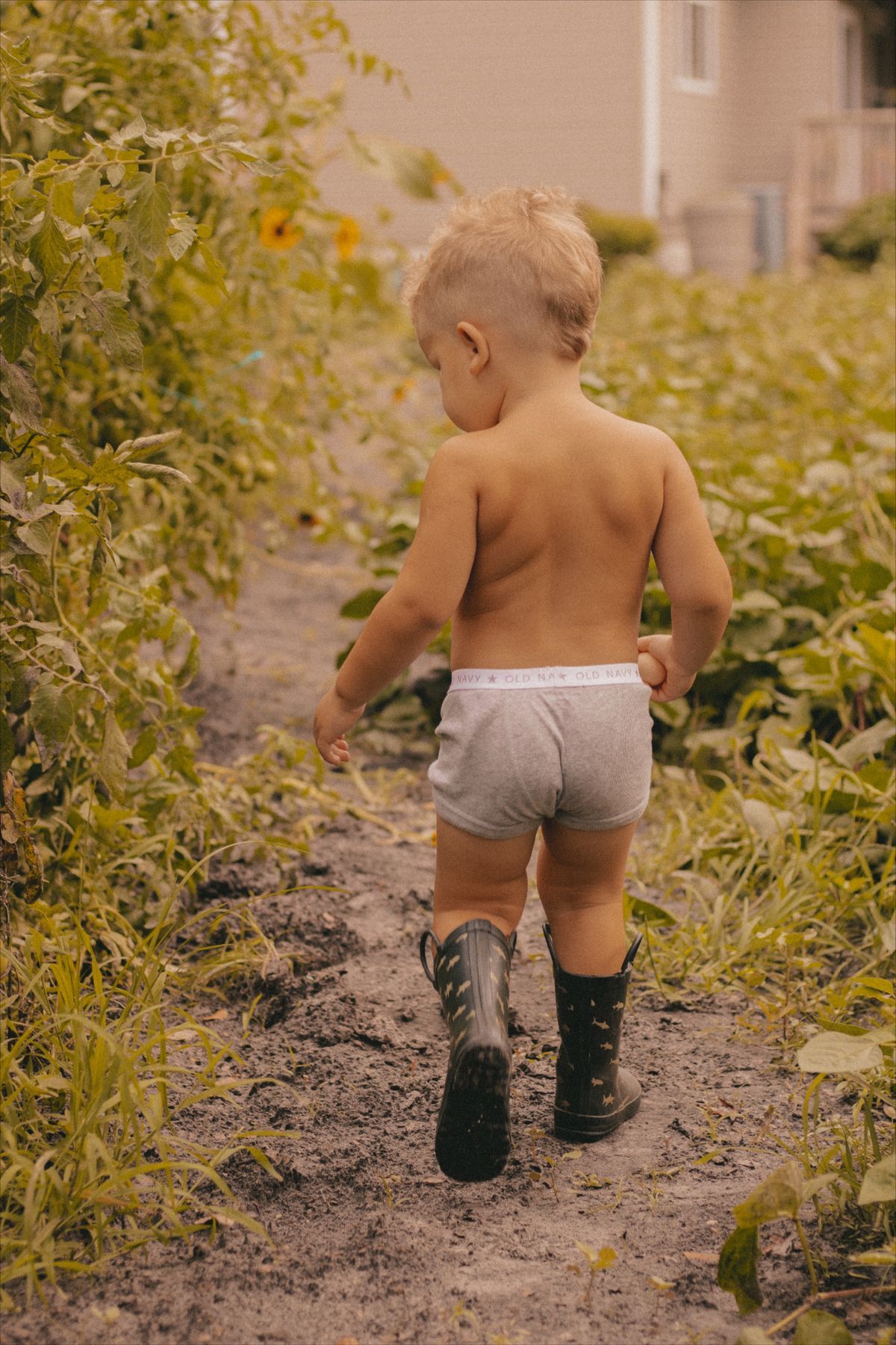 small child walking through a garden with rainboots on