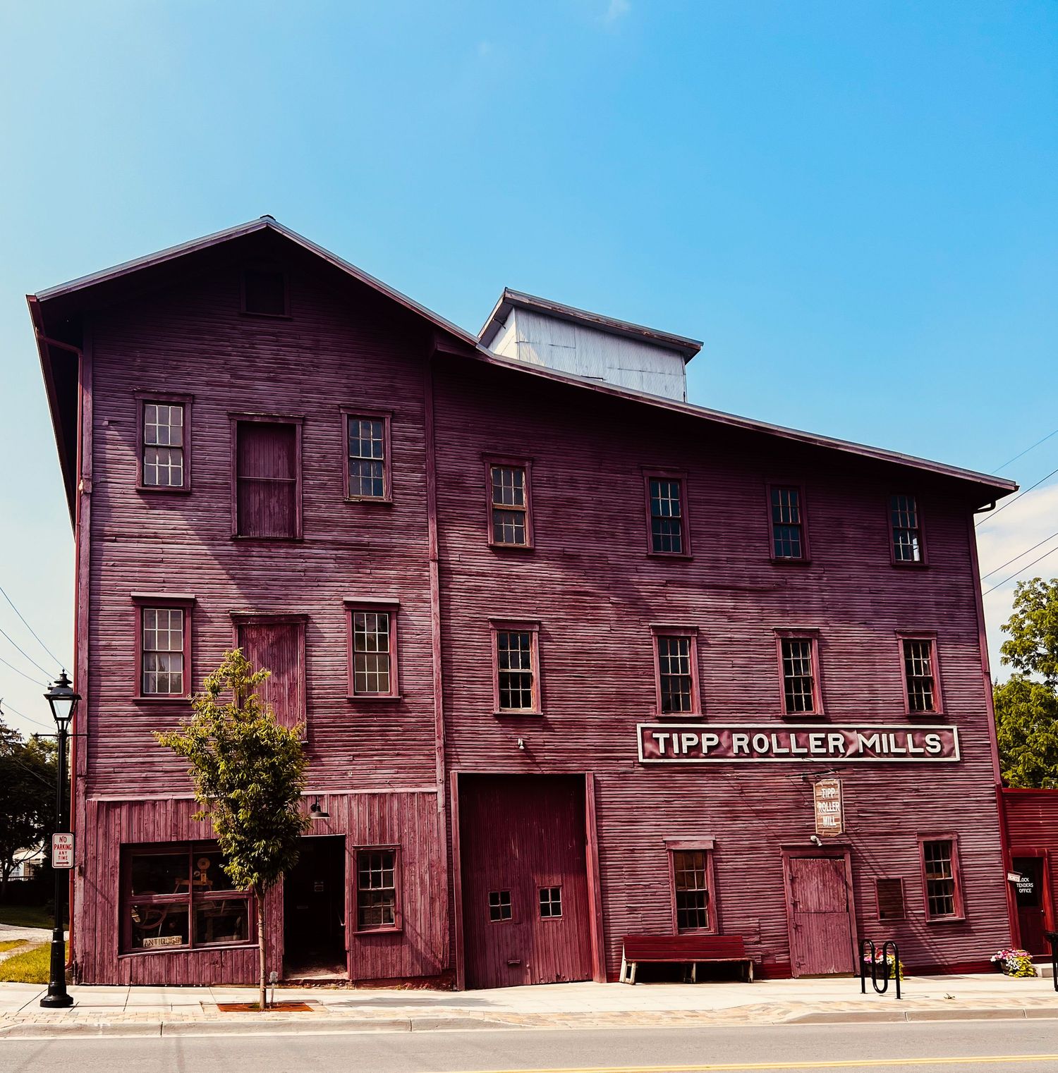 Historic Tipp Roller Mills building with red wooden exterior and multiple windows under a clear blue sky.