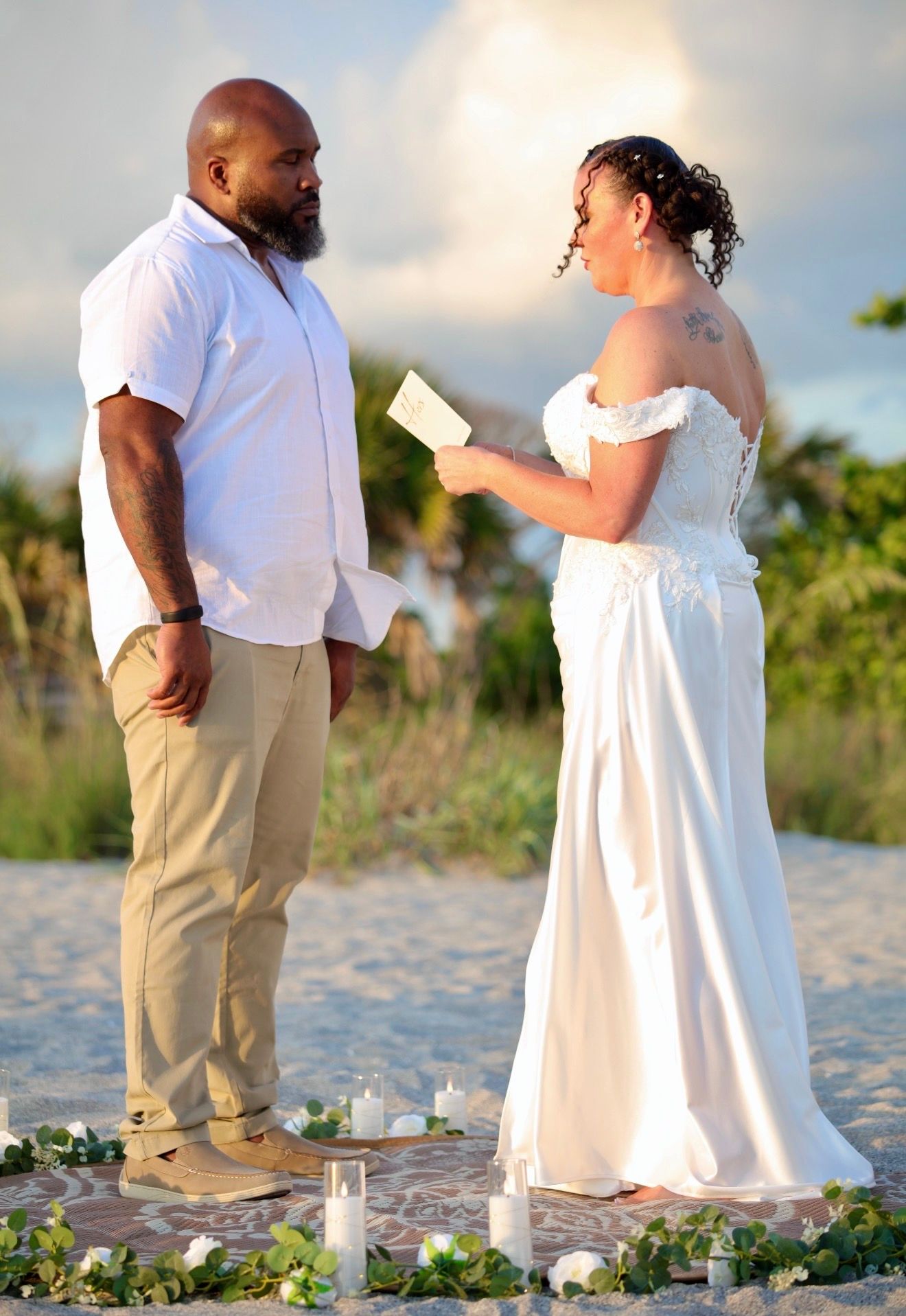Bride reads vows to groom during romantic beach wedding ceremony at sunset.