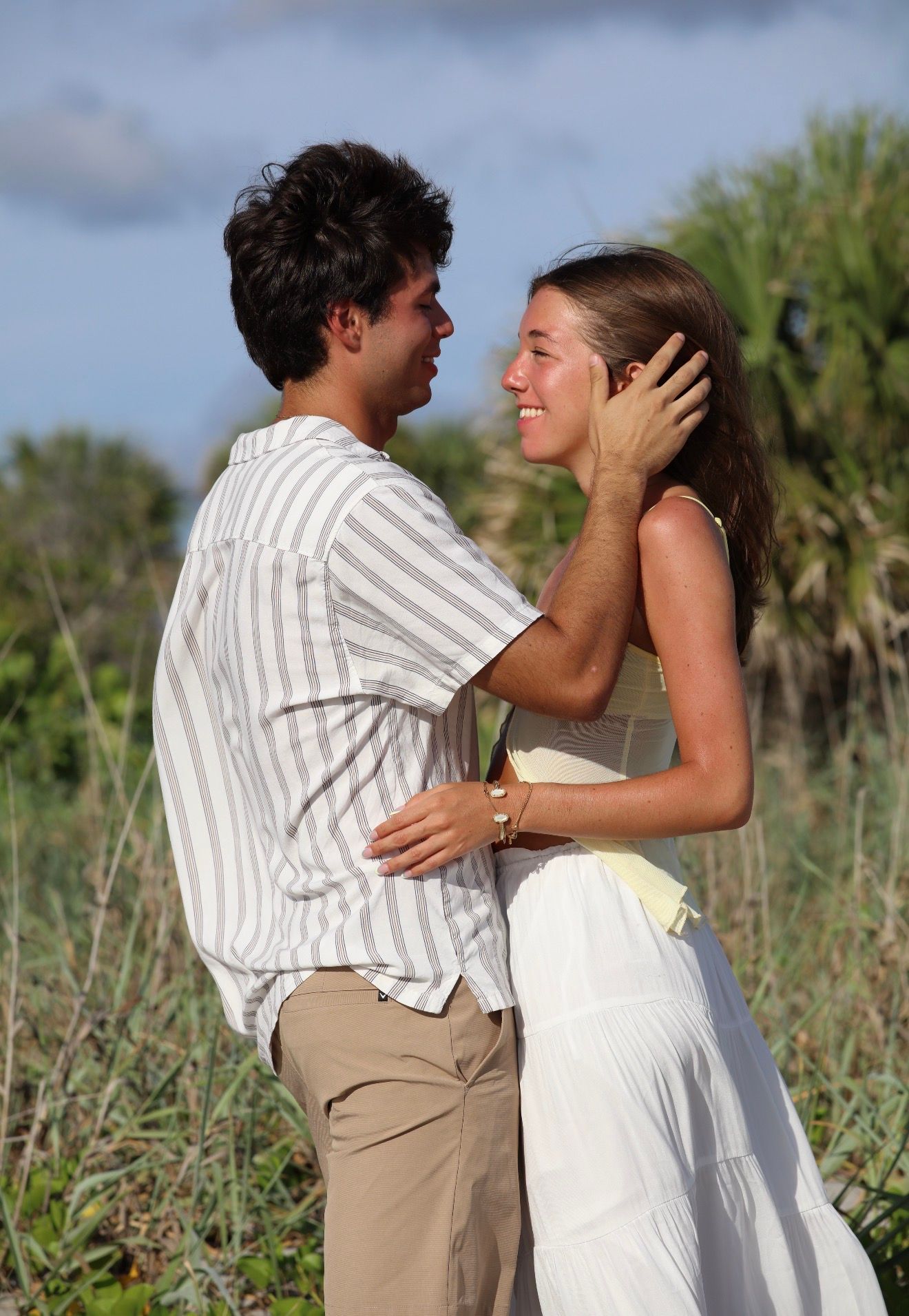 Young couple embracing romantically in a lush green field, man tenderly cupping woman's face.