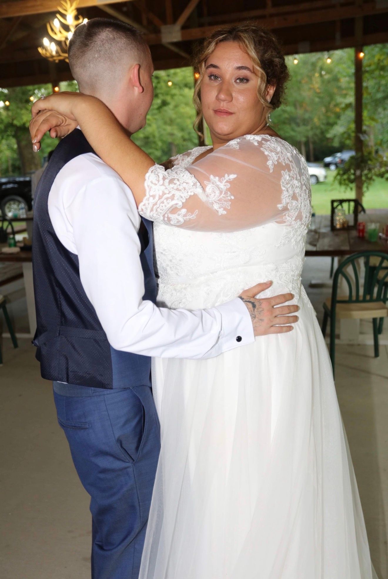 Bride in lace wedding gown shares first dance with groom in navy suit at outdoor wedding reception.