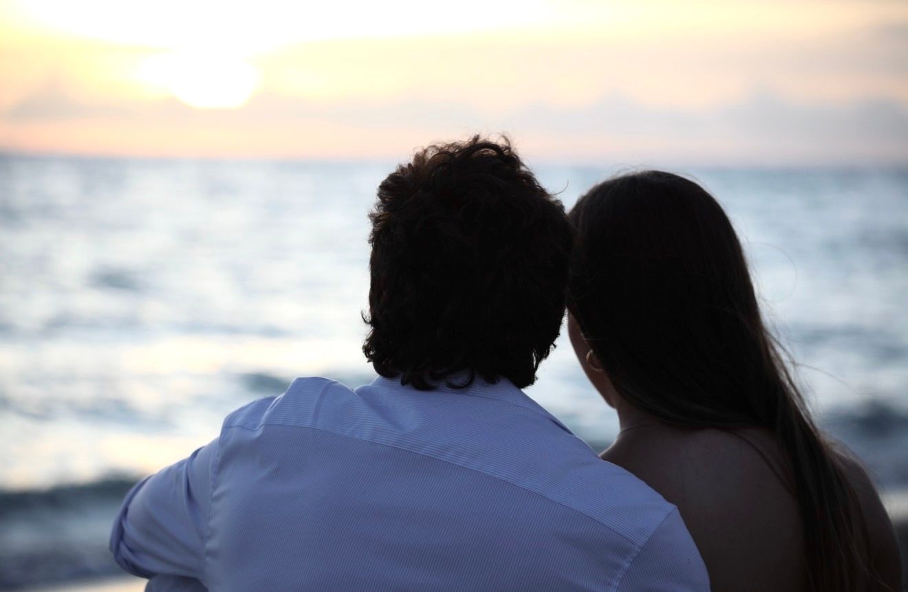 A couple sits together watching a romantic golden sunset over the calm ocean waters.