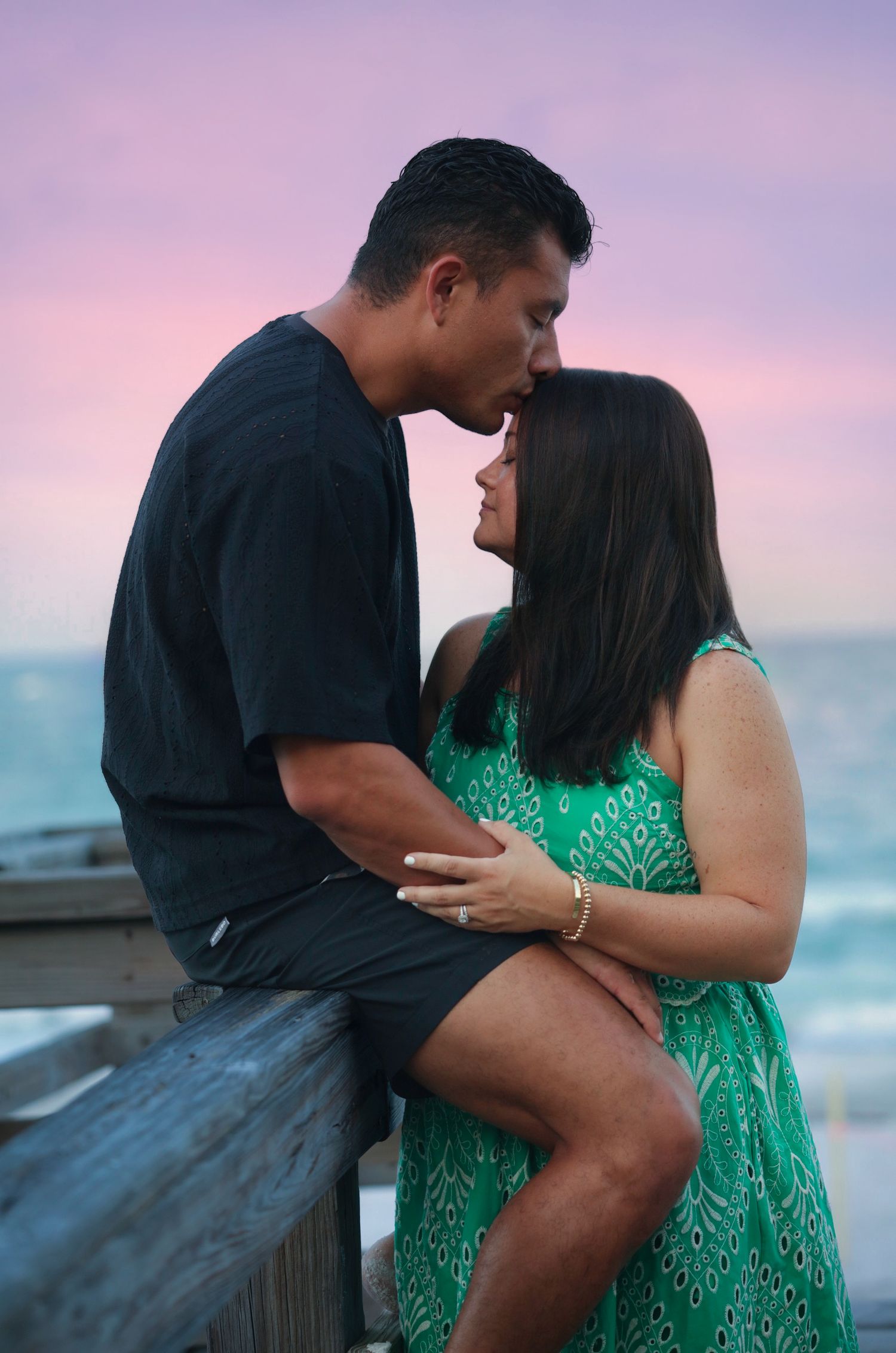 Romantic couple sharing a kiss on beach pier at sunset.