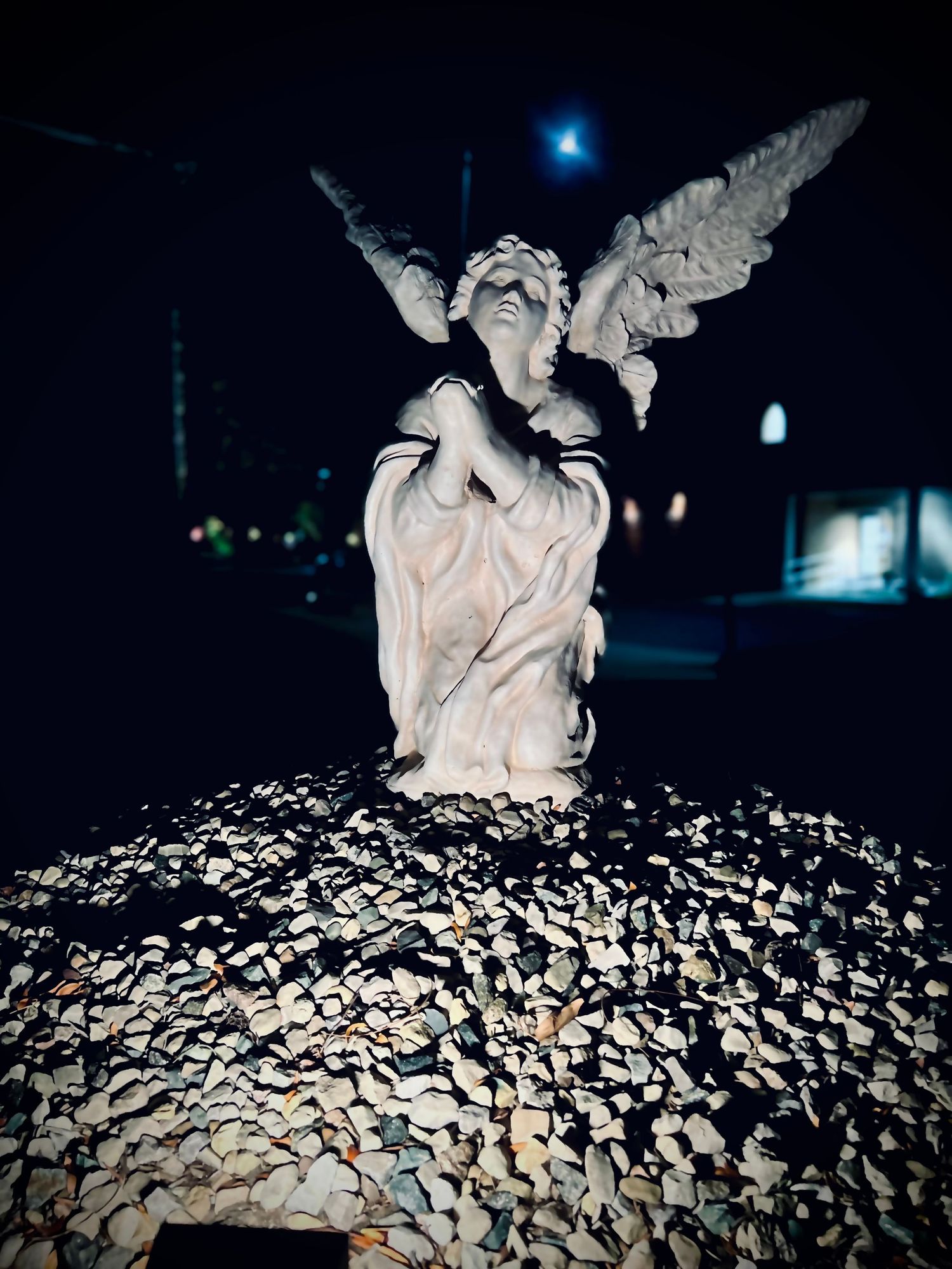 Stone angel statue with wings displayed outdoors at night, surrounded by scattered rocks and pebbles under moonlight.