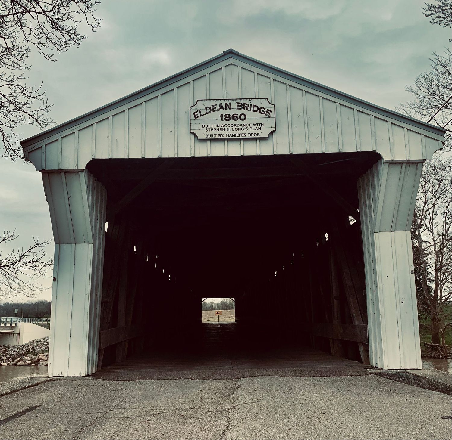 Historic Eldean Covered Bridge built in 1860, a white wooden structure with dark tunnel interior on a cloudy day.