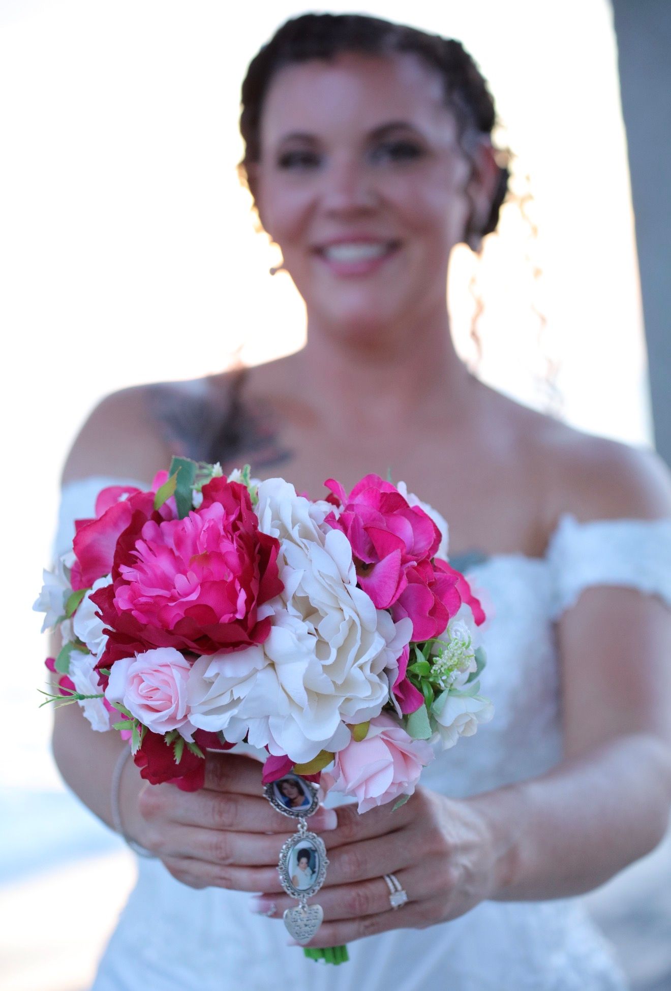 Bride in white strapless gown holds pink and white floral bouquet with memorial charm on her wedding day.