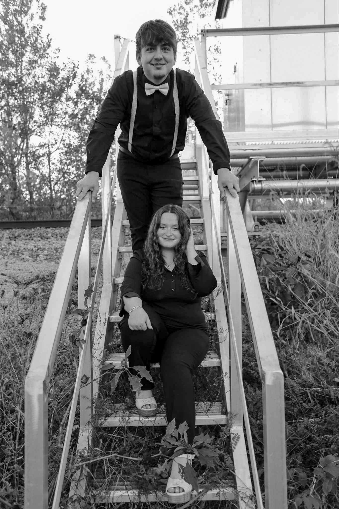 Black and white photo of a boy and girl in formal attire posing on outdoor metal stairs.