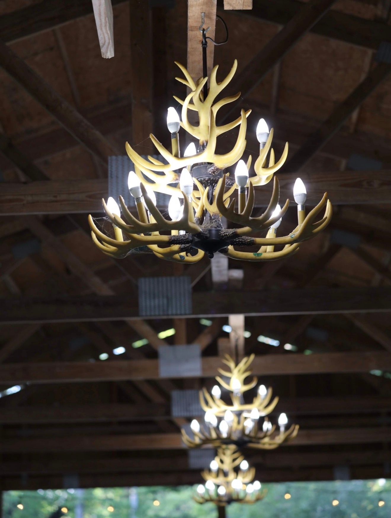 Rustic antler chandeliers hang from wooden beam ceiling at elegant barn wedding venue.