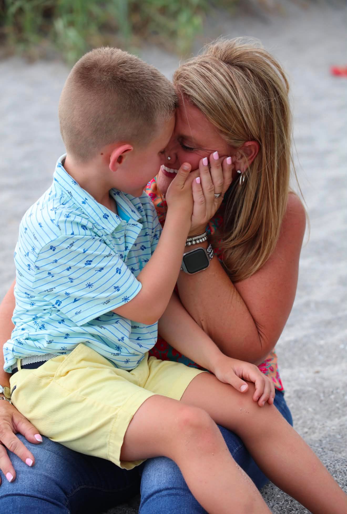 A young boy tenderly cups a smiling woman's face in his hands during a sweet outdoor moment together.