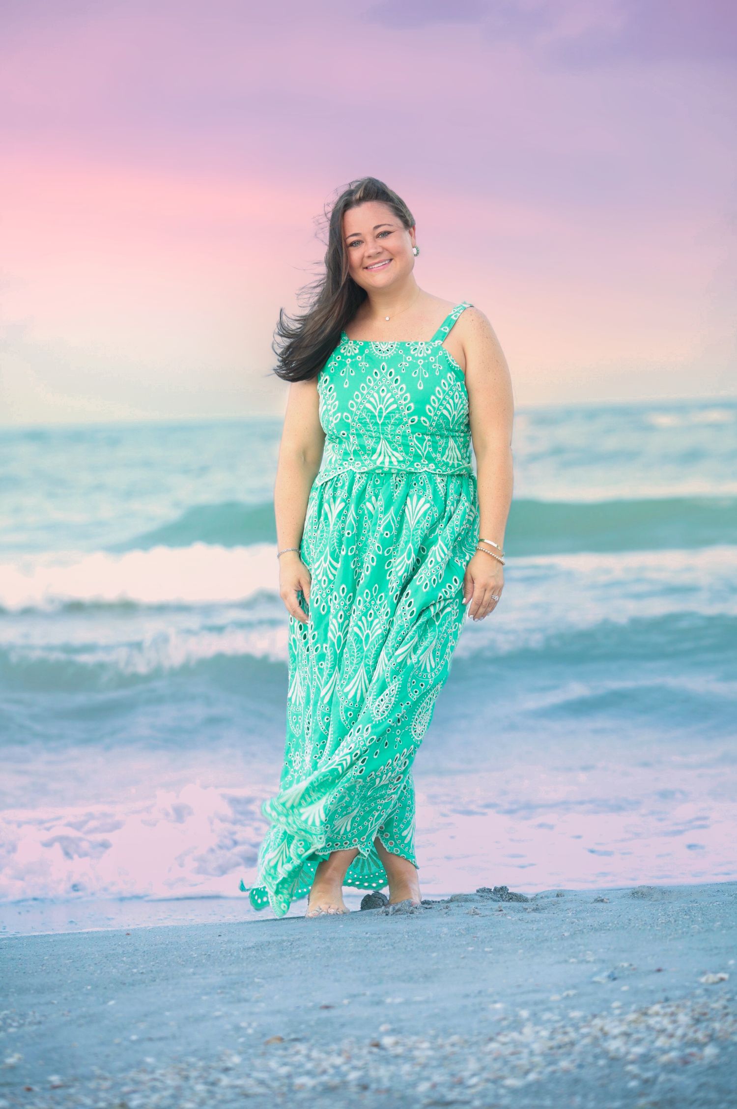 Woman in green maxi dress smiling on beach at sunset.
