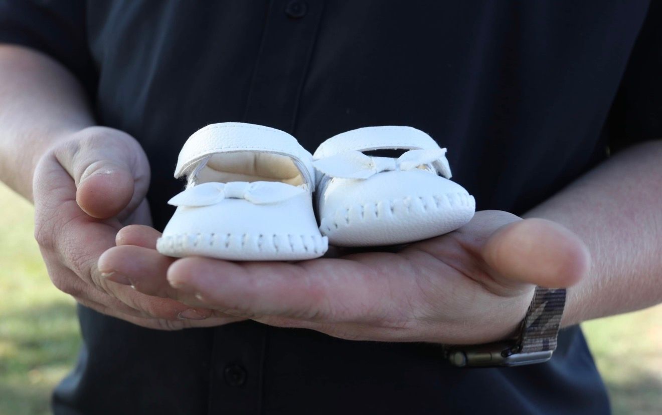 Man holding tiny white baby shoes in his hands outdoors.