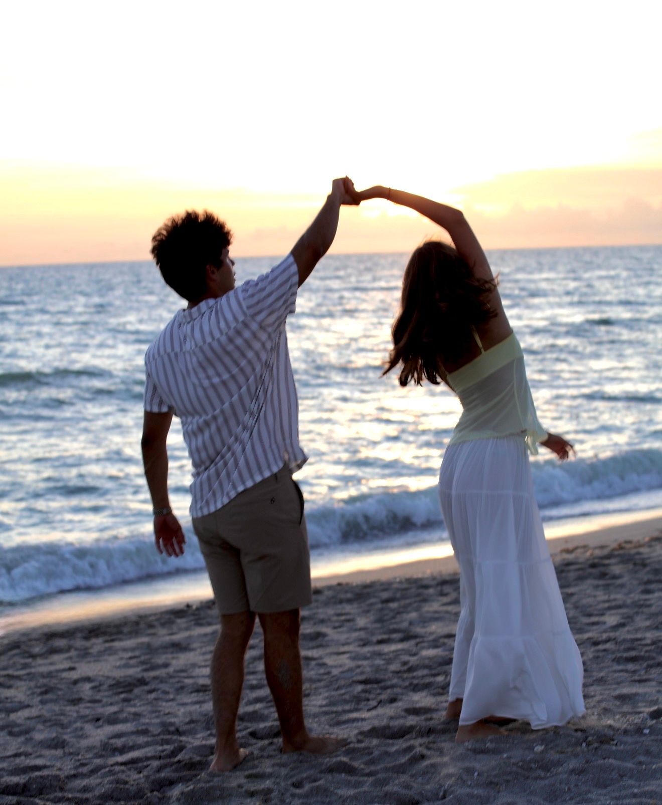 Couple dancing together on the beach at sunset, man spinning woman with hands raised overhead.