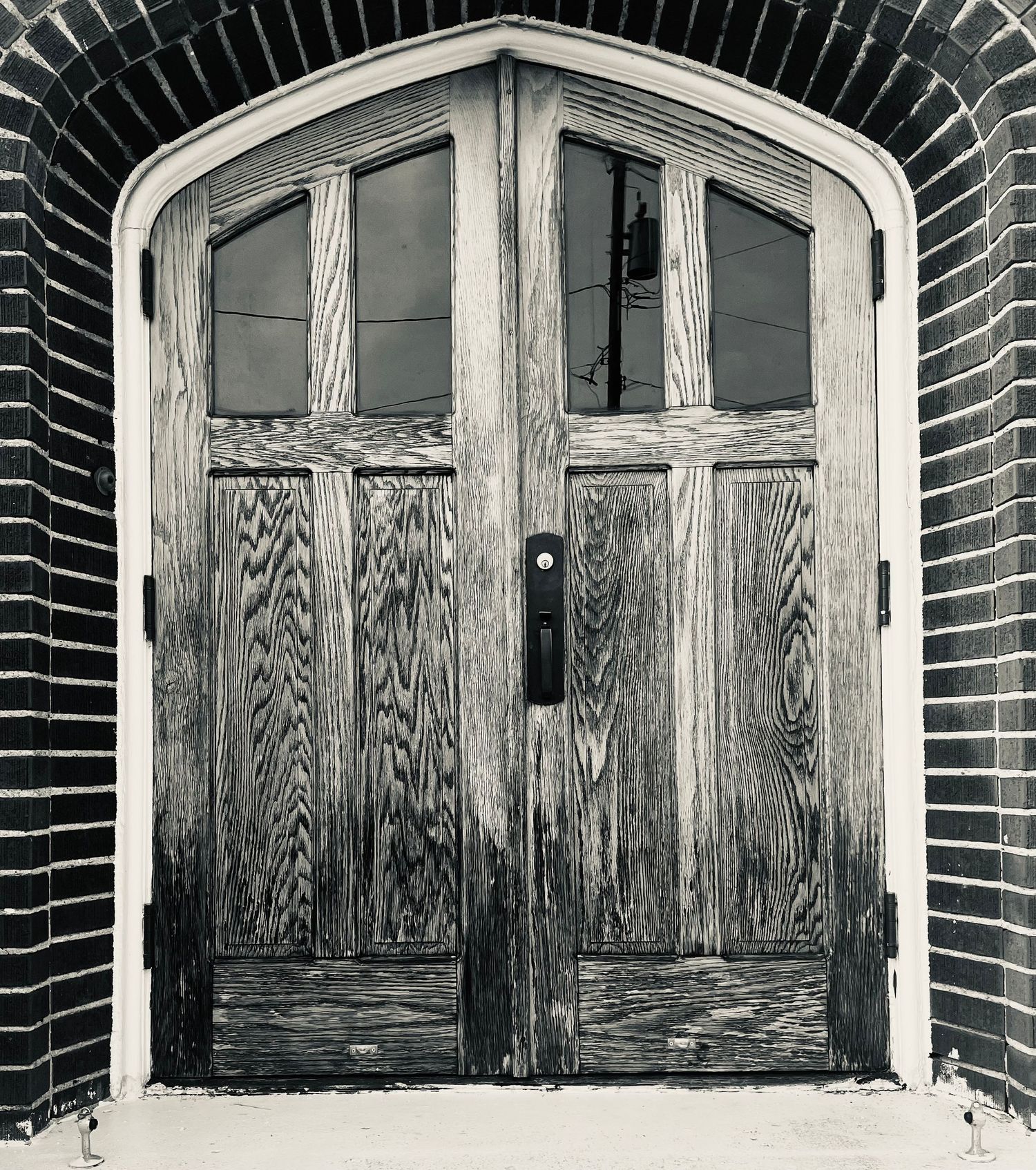 Black and white photo of weathered wooden double doors with arched brick surround and glass panels.