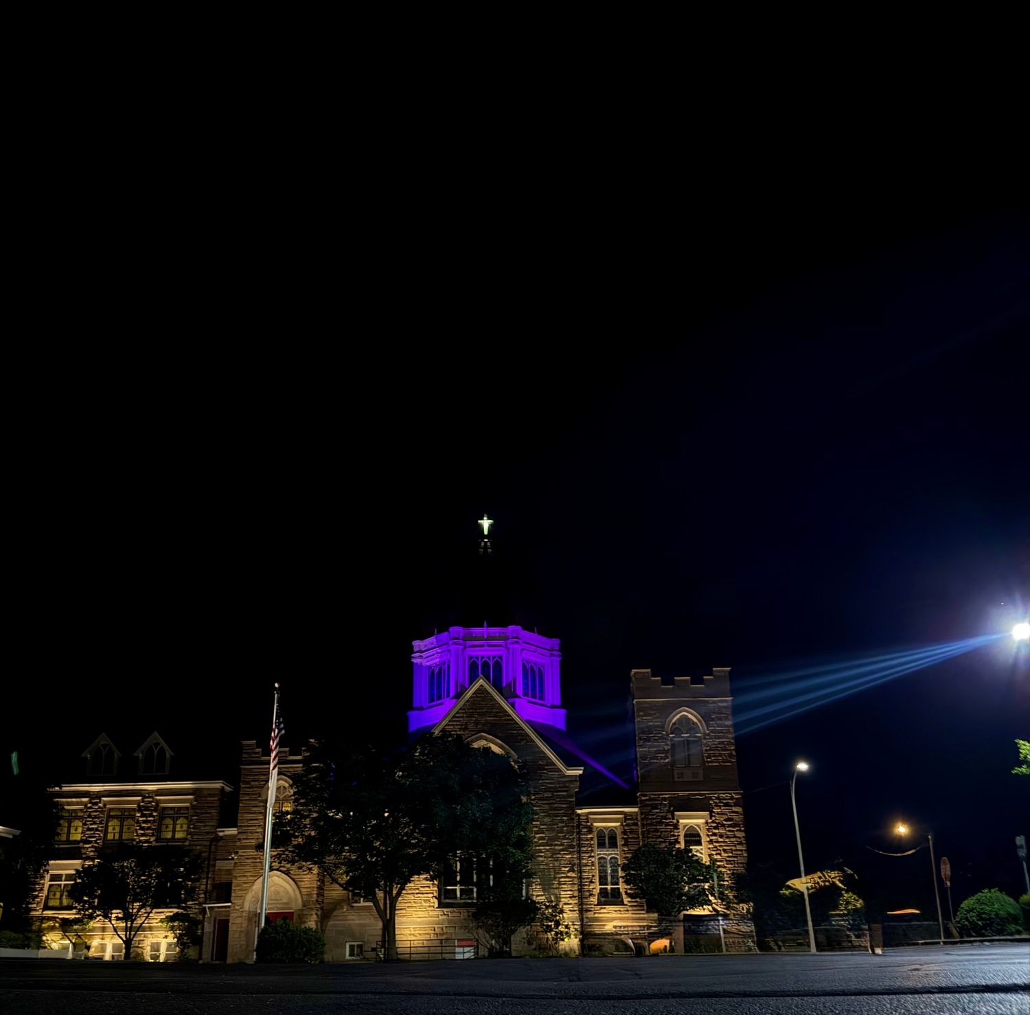 Historic stone church illuminated with purple lights at night, cross glowing atop the tower against a dark sky.