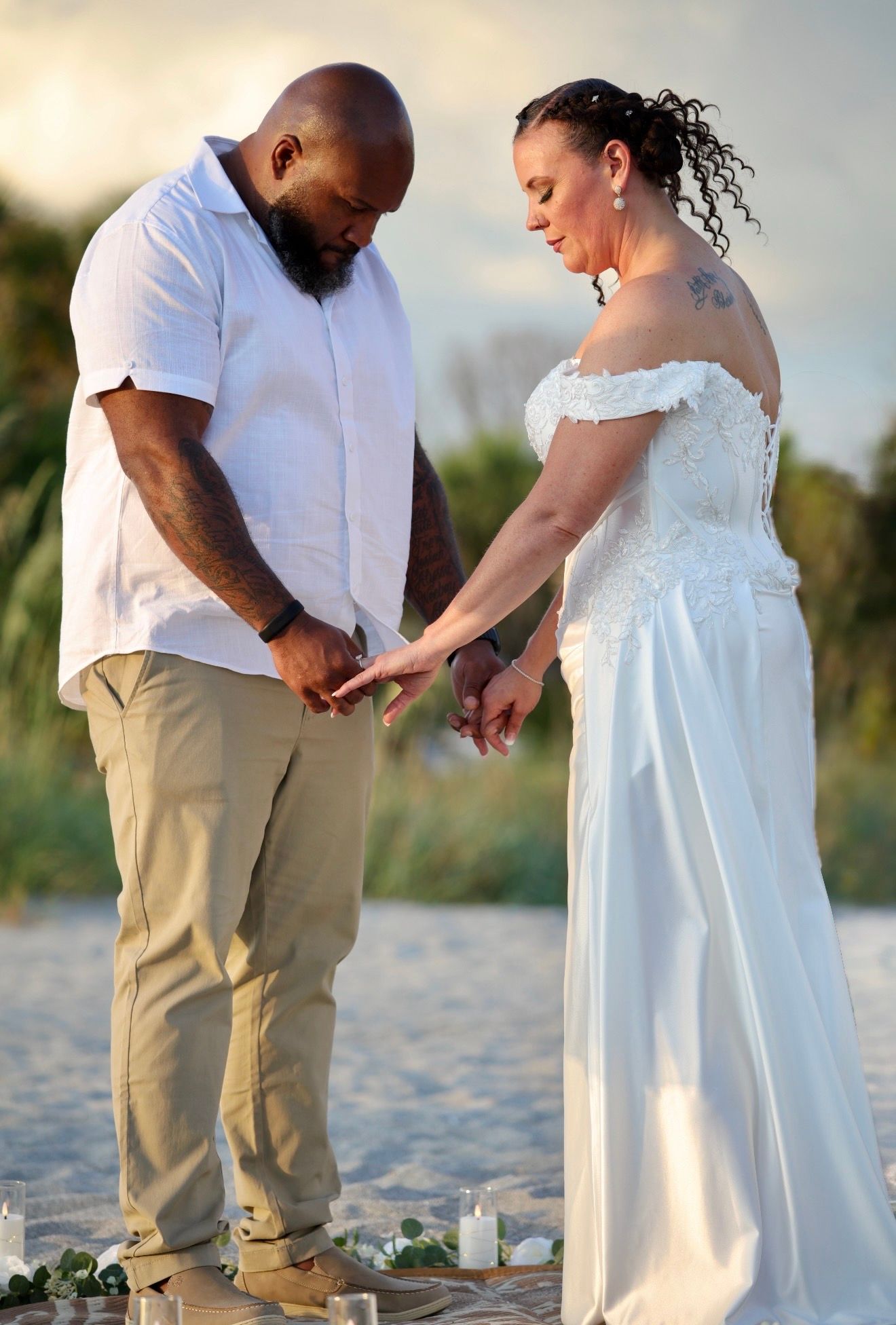 Bride and groom exchange rings during outdoor beach wedding ceremony with candles.