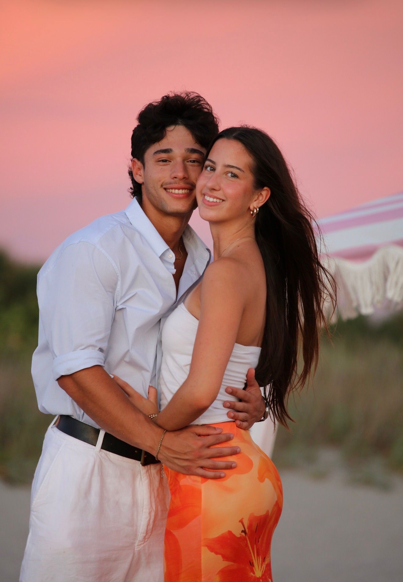 A young couple embraces on the beach during a vibrant pink and orange sunset.