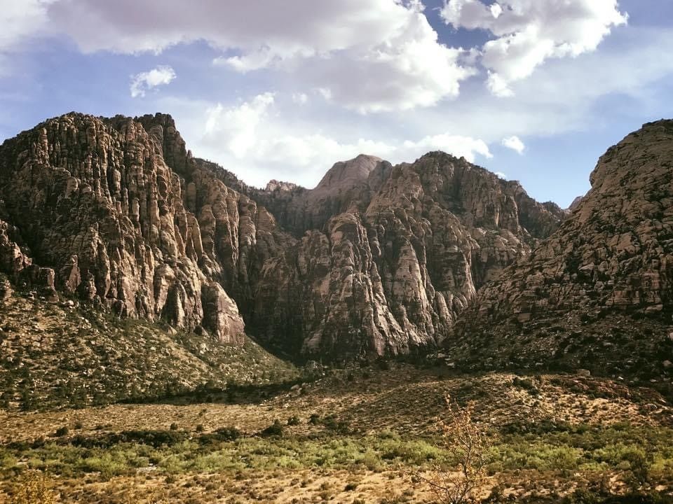 Rocky mountain canyon with rugged cliffs, desert shrubs, and a partly cloudy sky in an arid landscape.