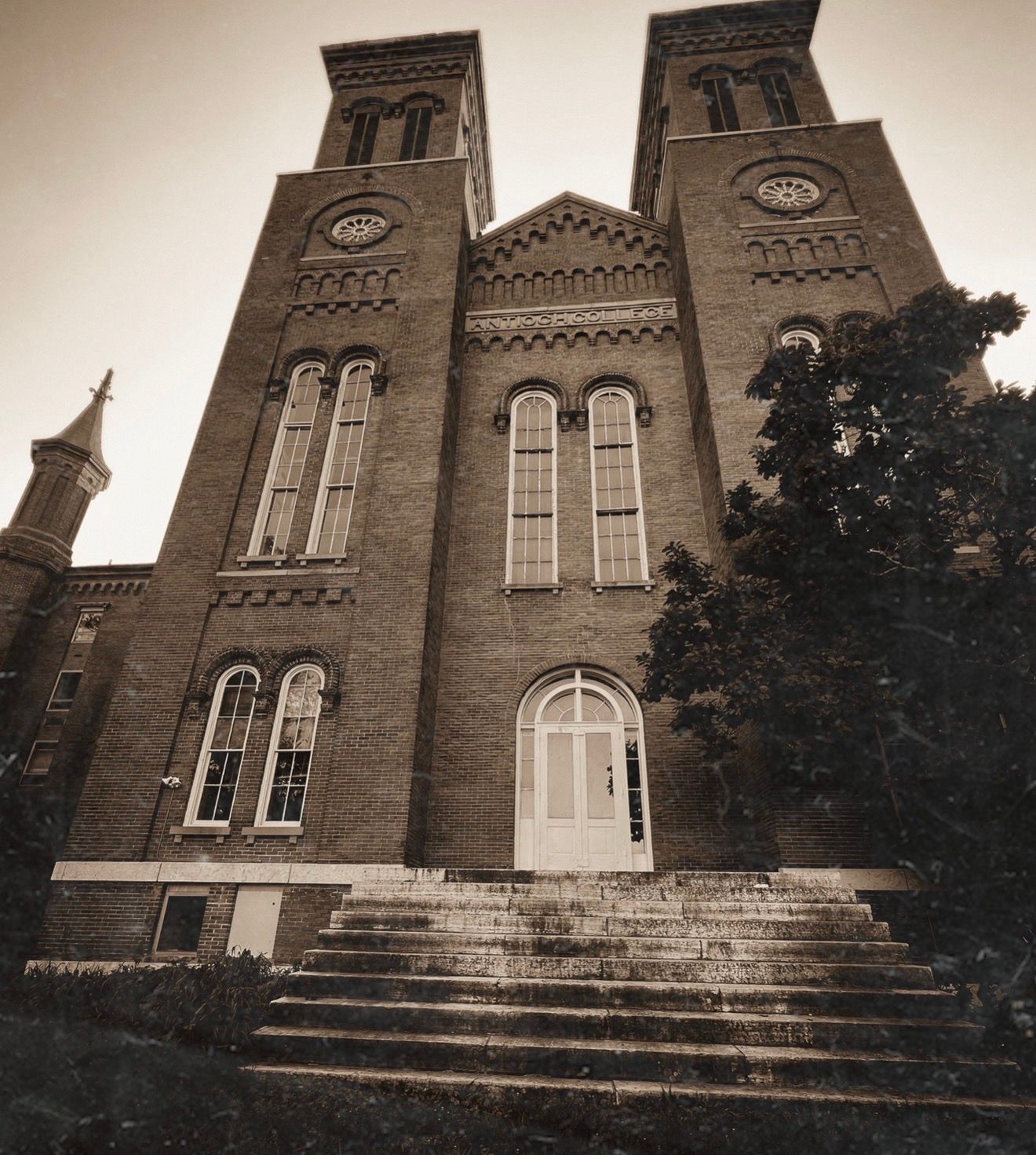 Sepia-toned historic brick church with twin towers, arched windows, and stone steps leading to a white entrance door.