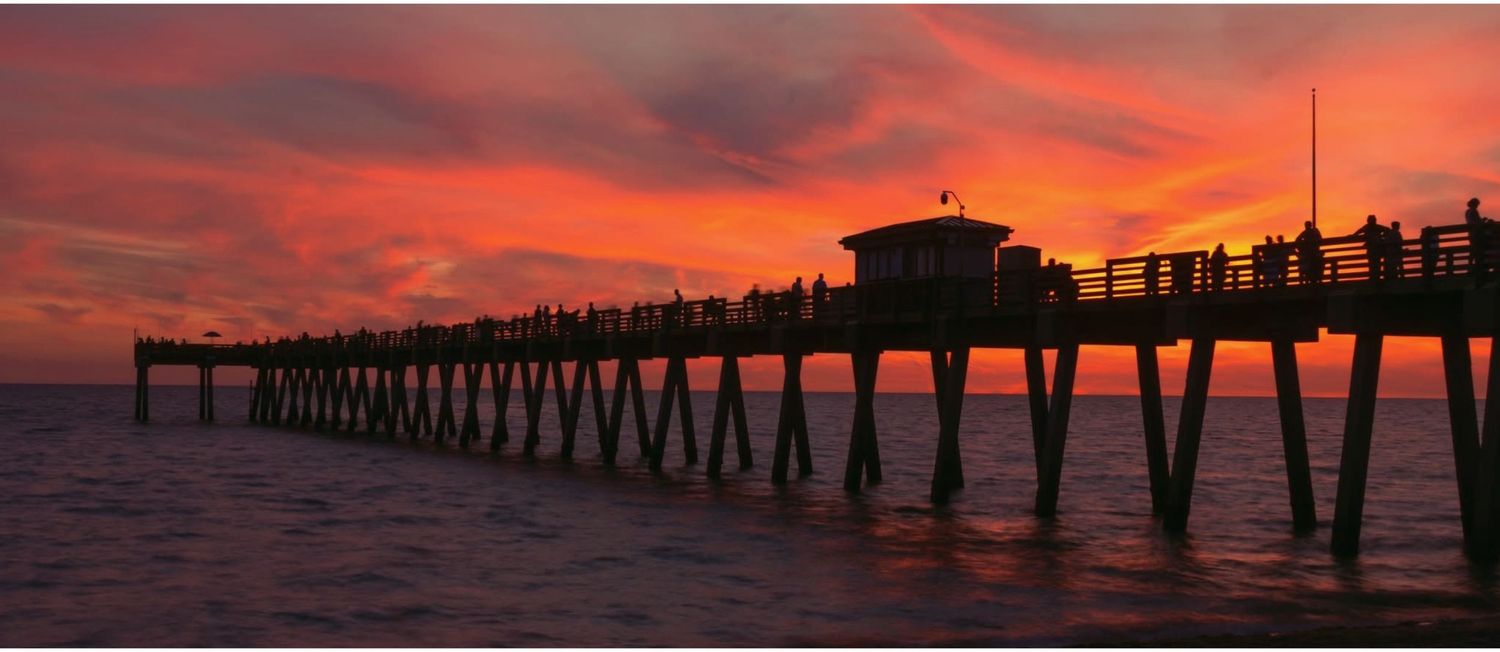 Stunning panoramic sunset view of a wooden ocean pier silhouetted against a vibrant red and orange sky.
