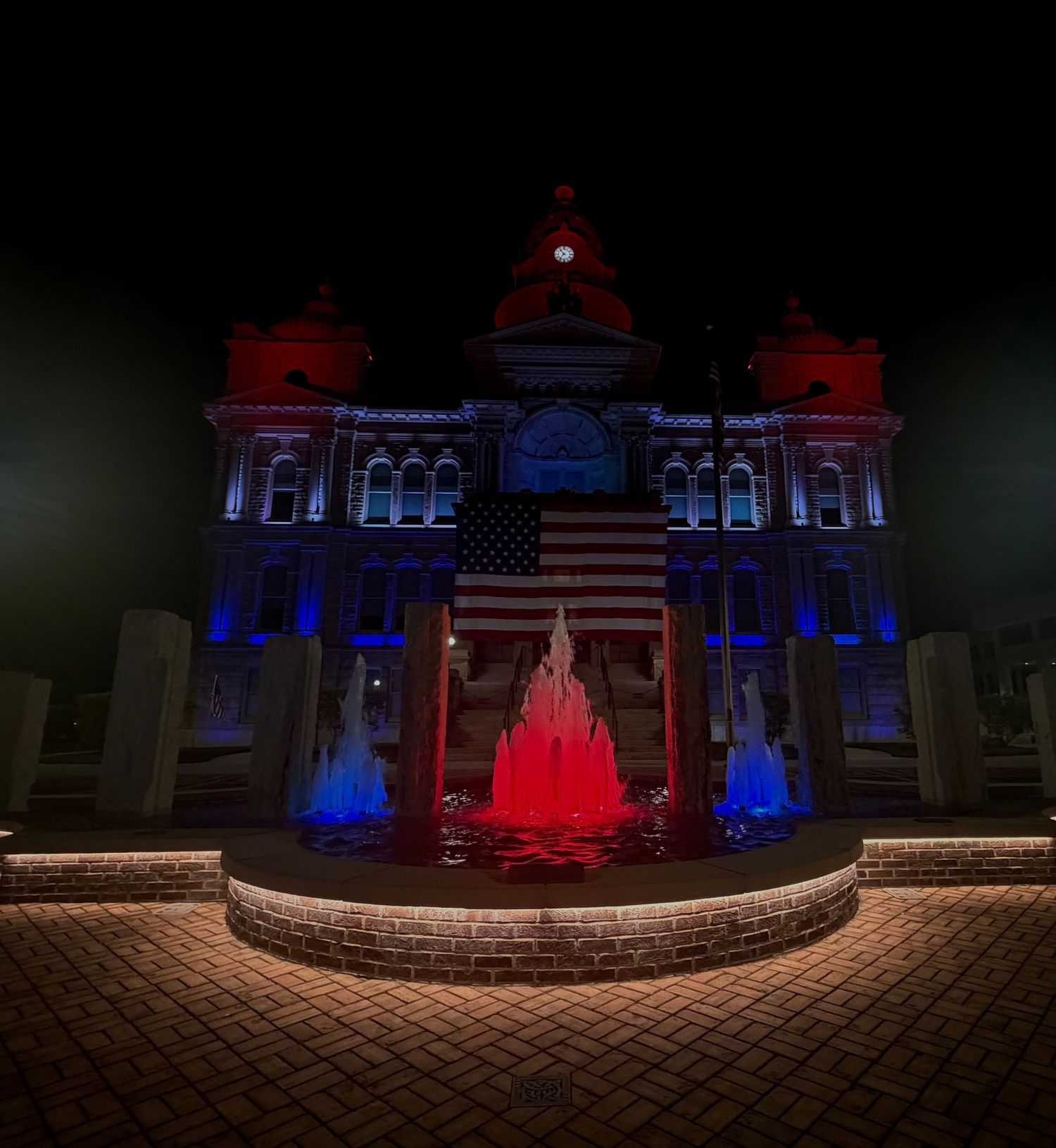Historic building illuminated in red, white, and blue lights with a fountain and American flag at night.