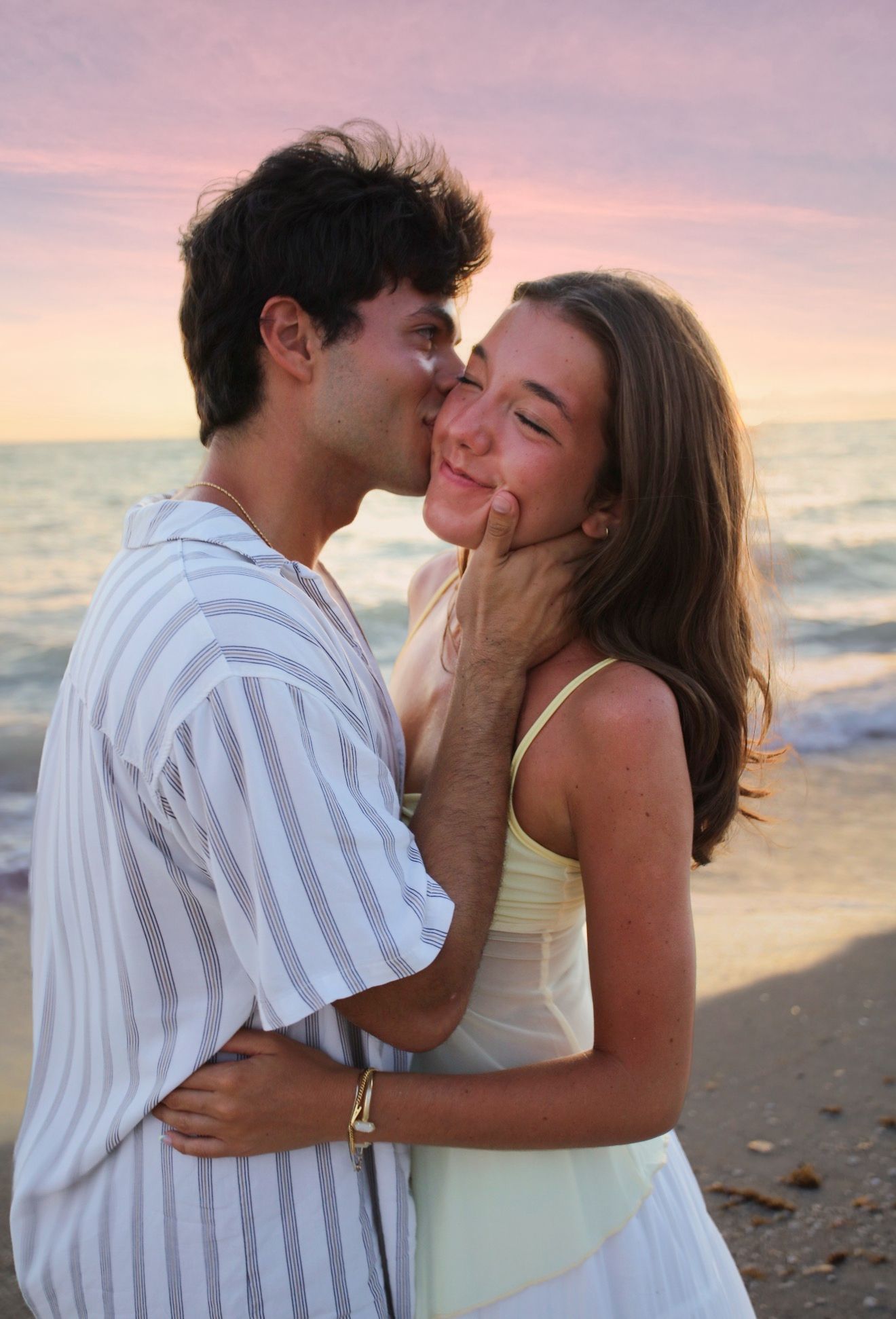 Young couple sharing a tender kiss on the beach during a beautiful pink and purple sunset.