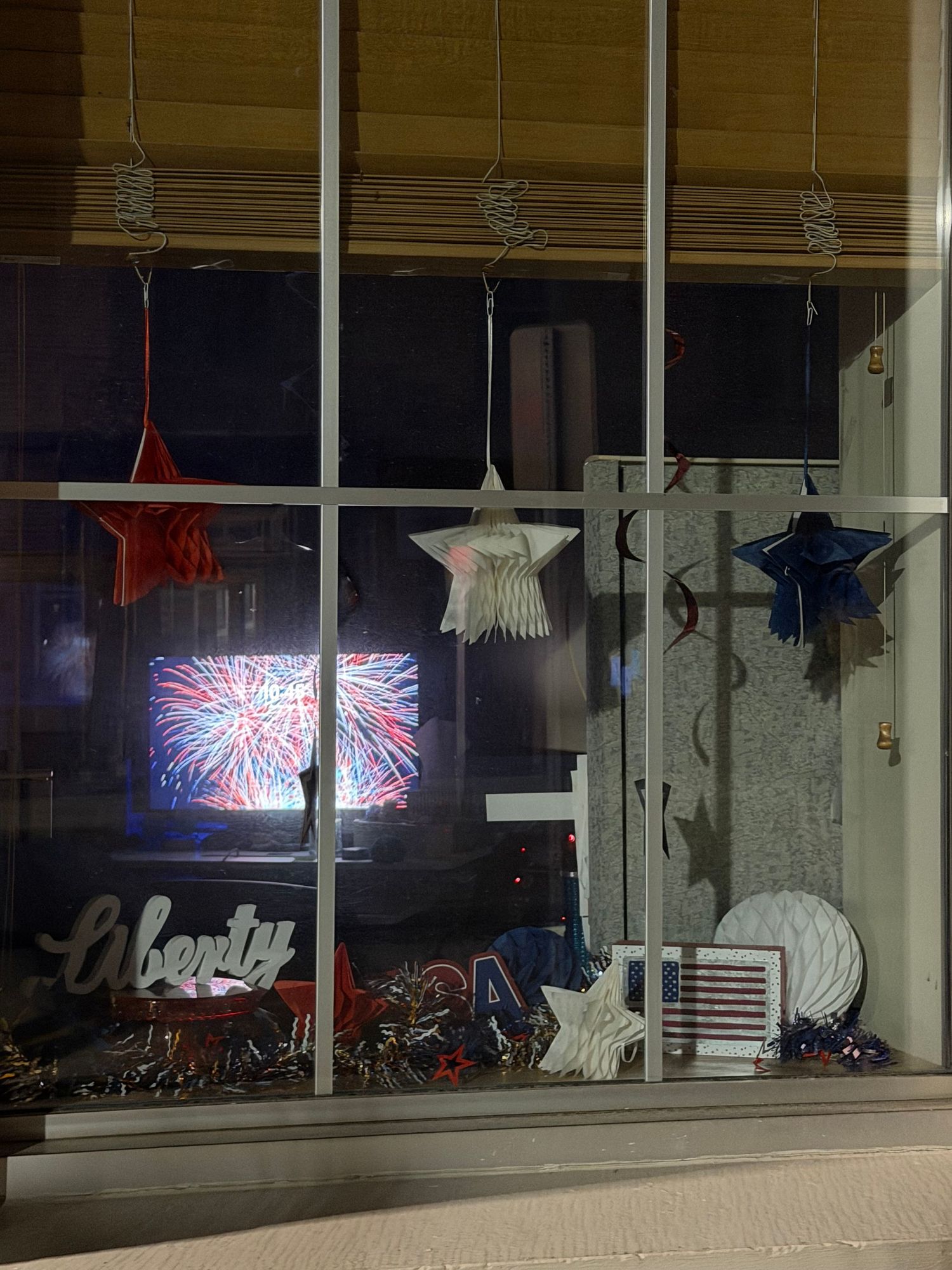 Patriotic window display with Liberty sign, star decorations, and fireworks TV screen at night.