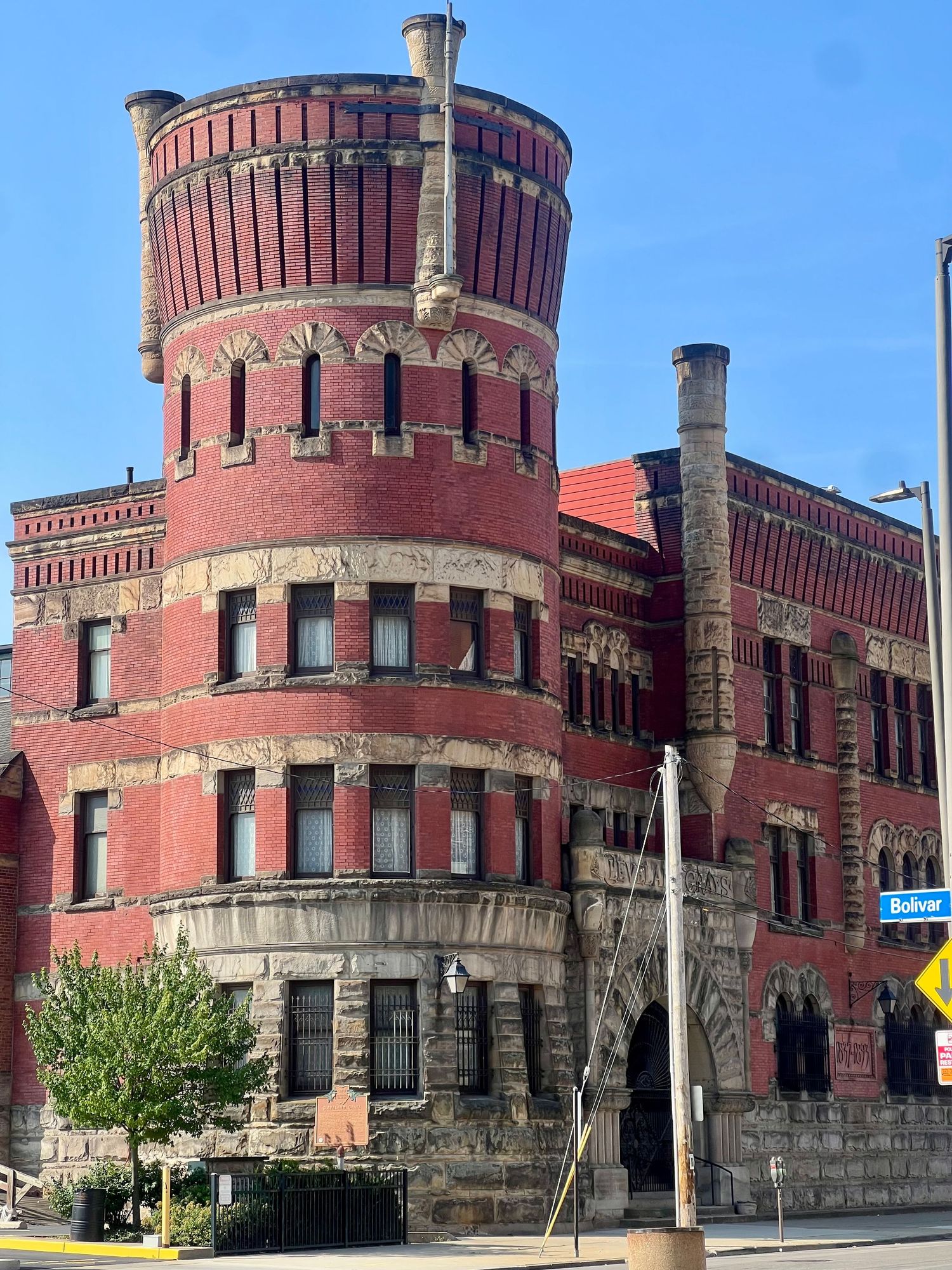 Historic red brick Romanesque Revival building with cylindrical tower, ornate stone details, and arched windows on a sunny day.